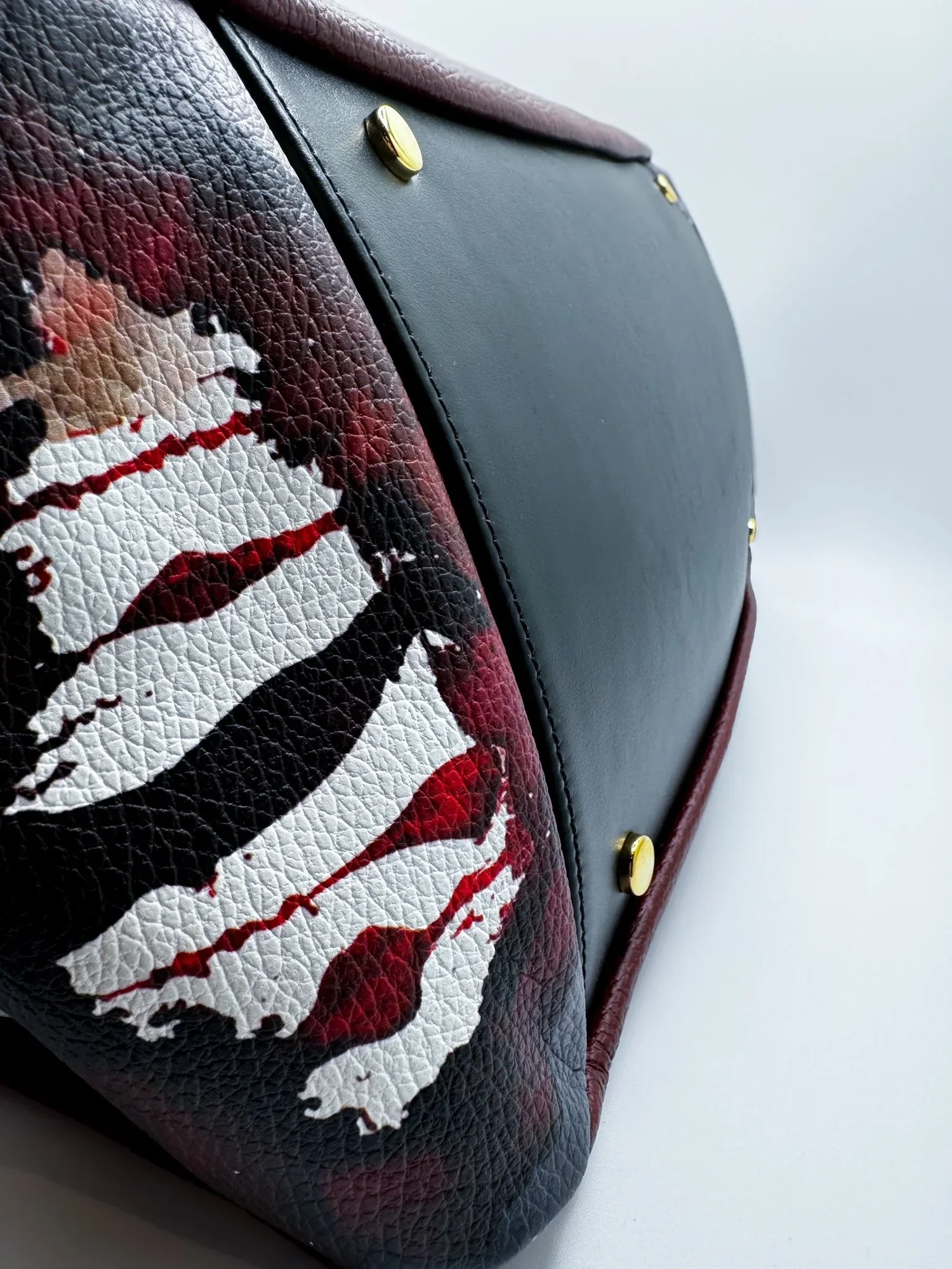 Close up image of a maroon colored leather Handbag, the bottom with black leather, sitting on a white background.