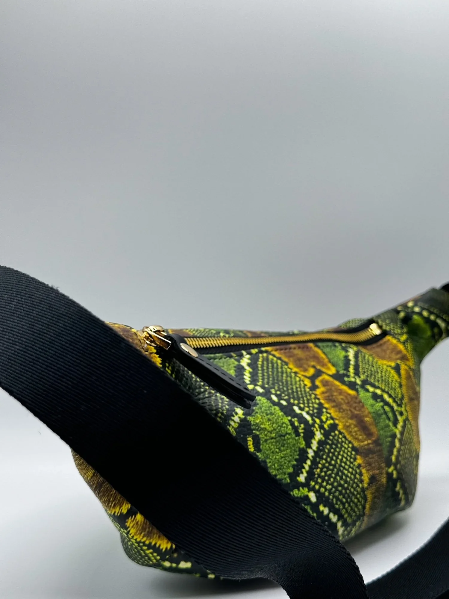 Close up photo of a green and black textured snakeskin print fanny pack, on a white surface.