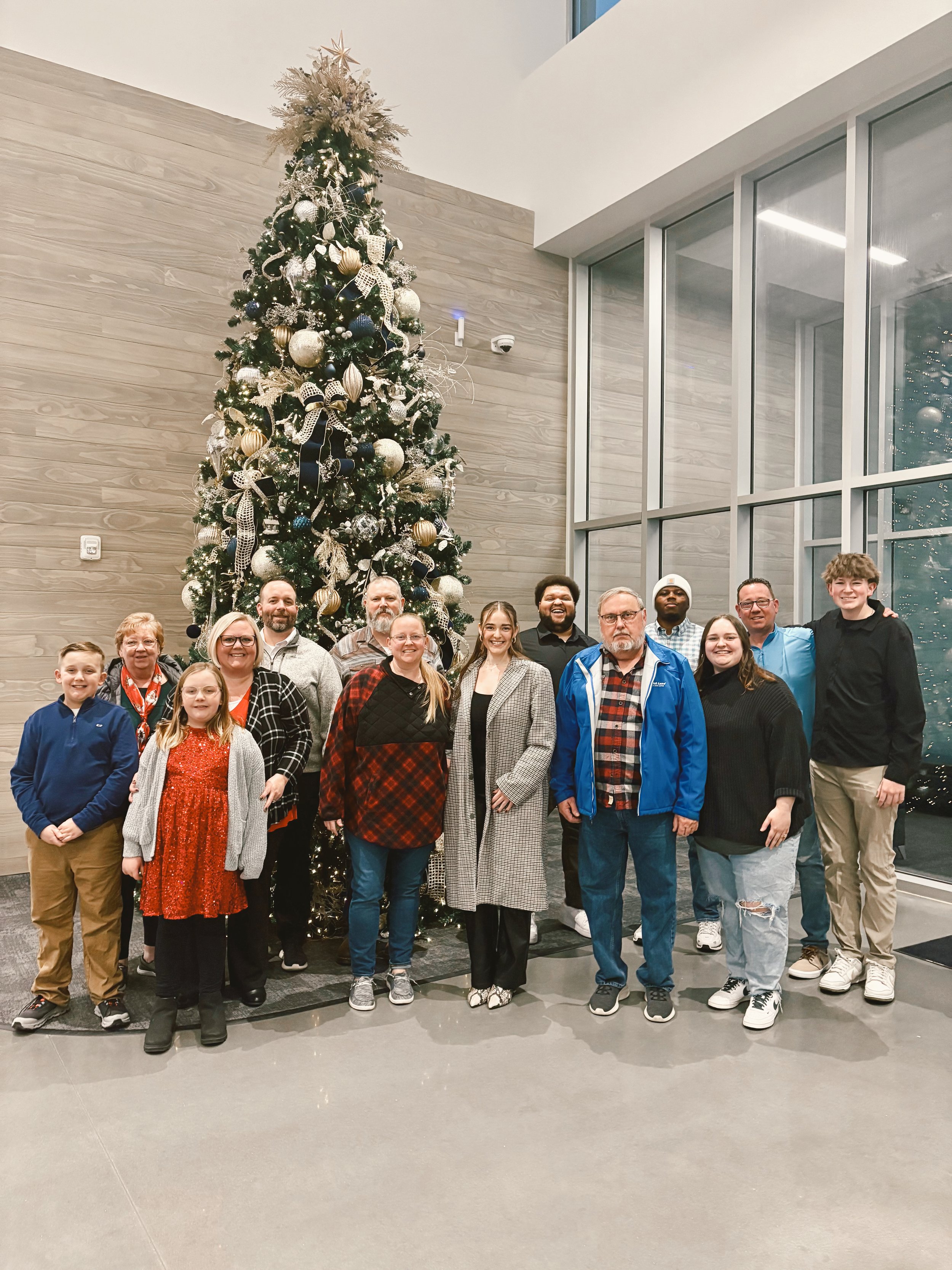 Group of people standing in front of a decorated Christmas tree indoors.