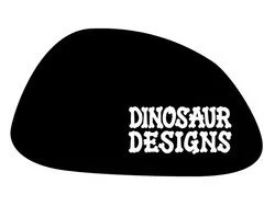 A black guitar pick with white text that says 'DINOSAUR DESIGNS'.