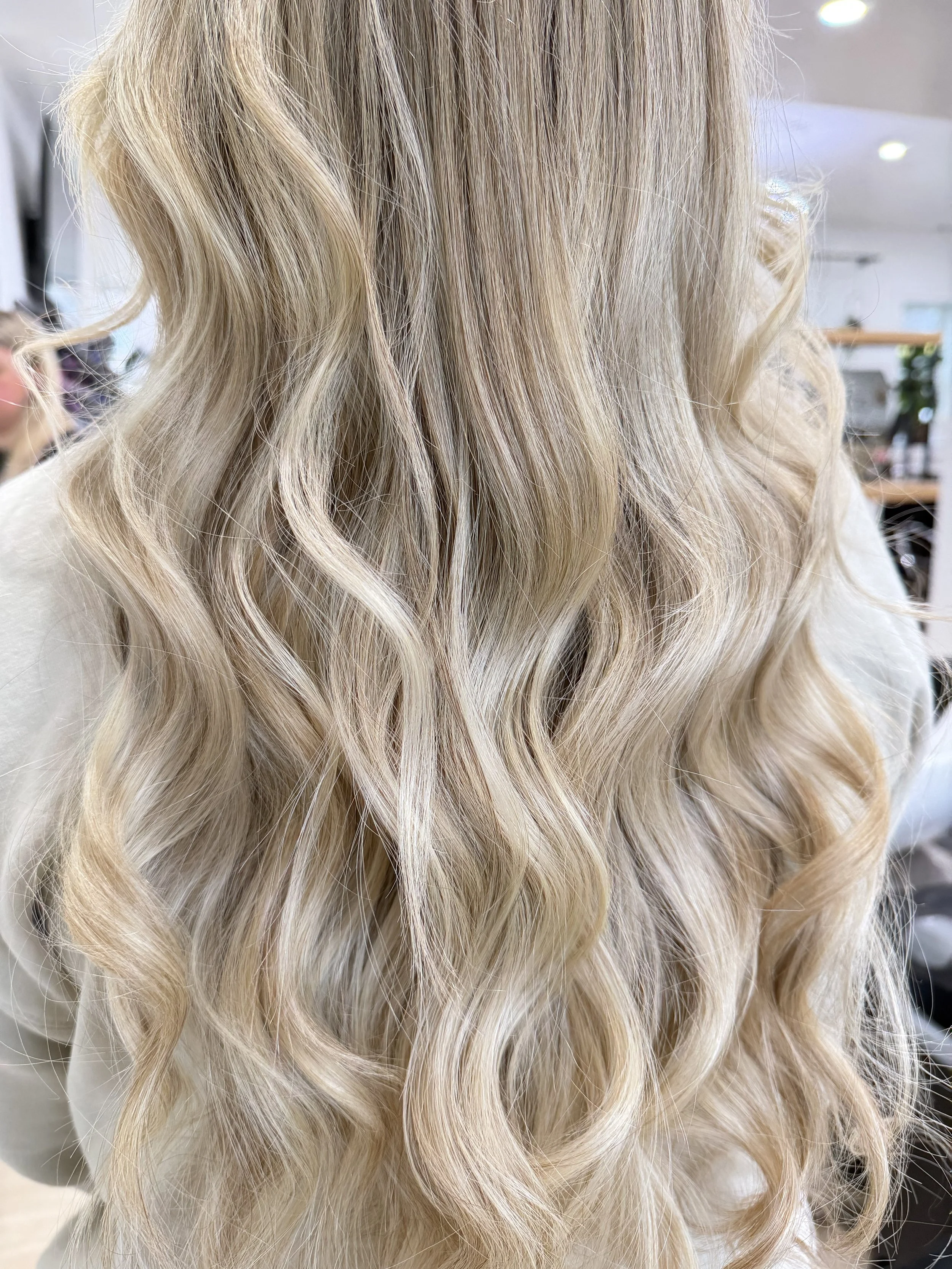 Close-up of long, wavy blonde hair with highlights, styled in soft curls.