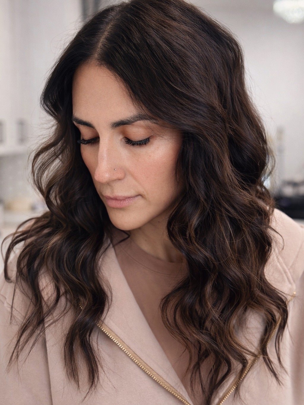 A woman with long, wavy, dark brown hair looking downward.