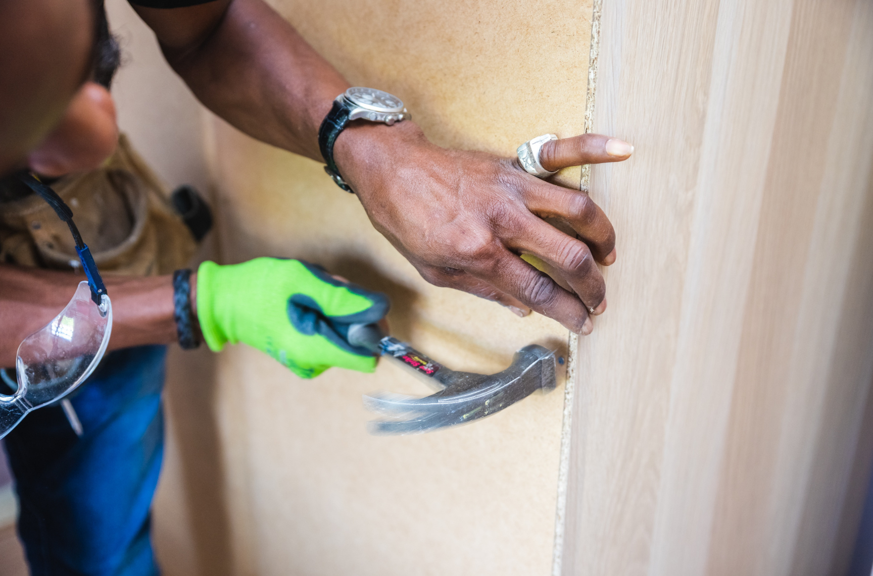 Person installing a wooden panel, wearing green gloves and using a hammer.