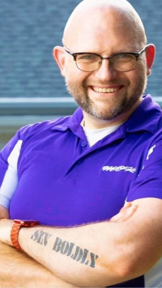 Matthew D. Kauffmann, founder of mIsFiTs Like ME, smiling with arms crossed, forearm tattoo reading "Sin Boldly" visible — St. Louis boudoir and erotic art photographer, Lebanon Illinois.
