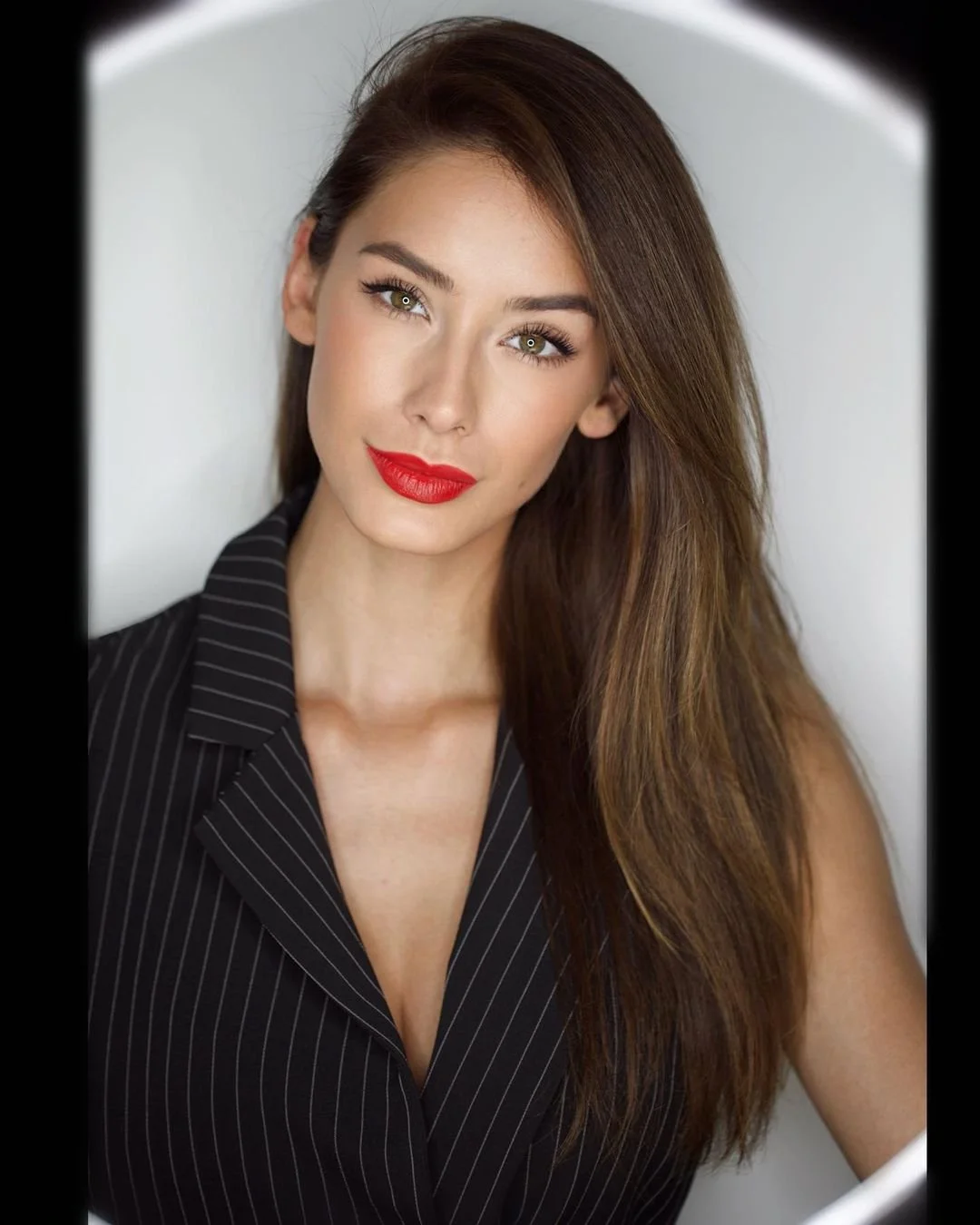 Woman with long hair and red lipstick wearing a pinstripe blazer, looking directly at the camera.