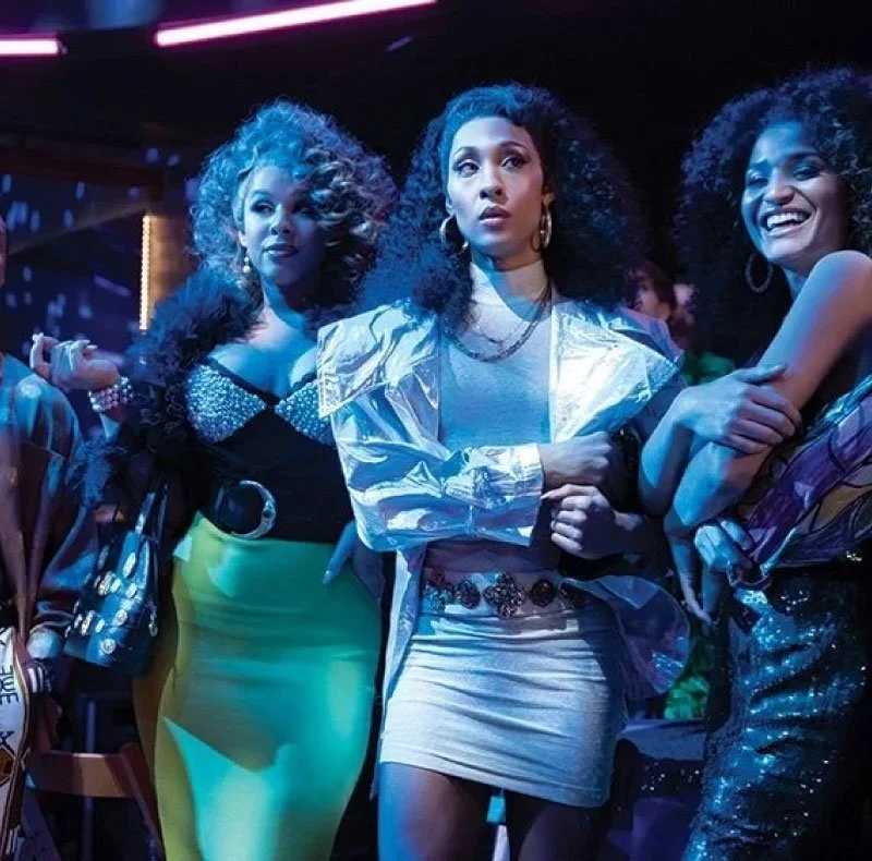 Three women with curly hair at a party or social event, illuminated with purple and blue lighting.