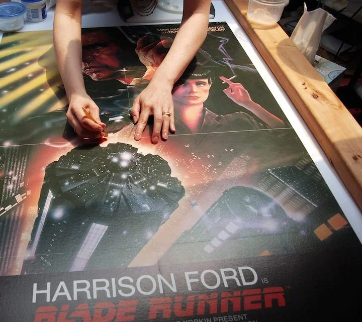 Person signing a "Blade Runner" movie poster on a table.