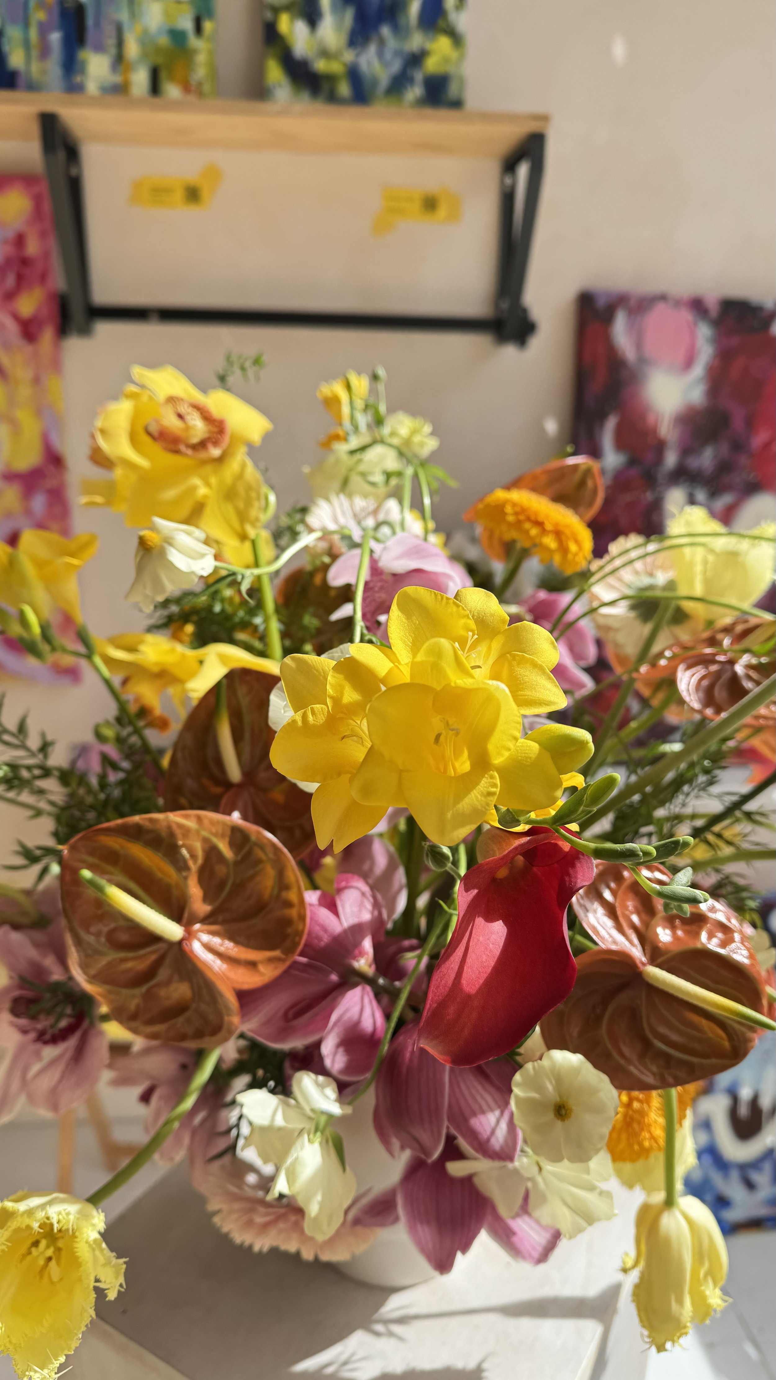 A vibrant bouquet of mixed flowers including yellow, pink, white, and orange blossoms in a white vase, sunlight illuminating the arrangement.