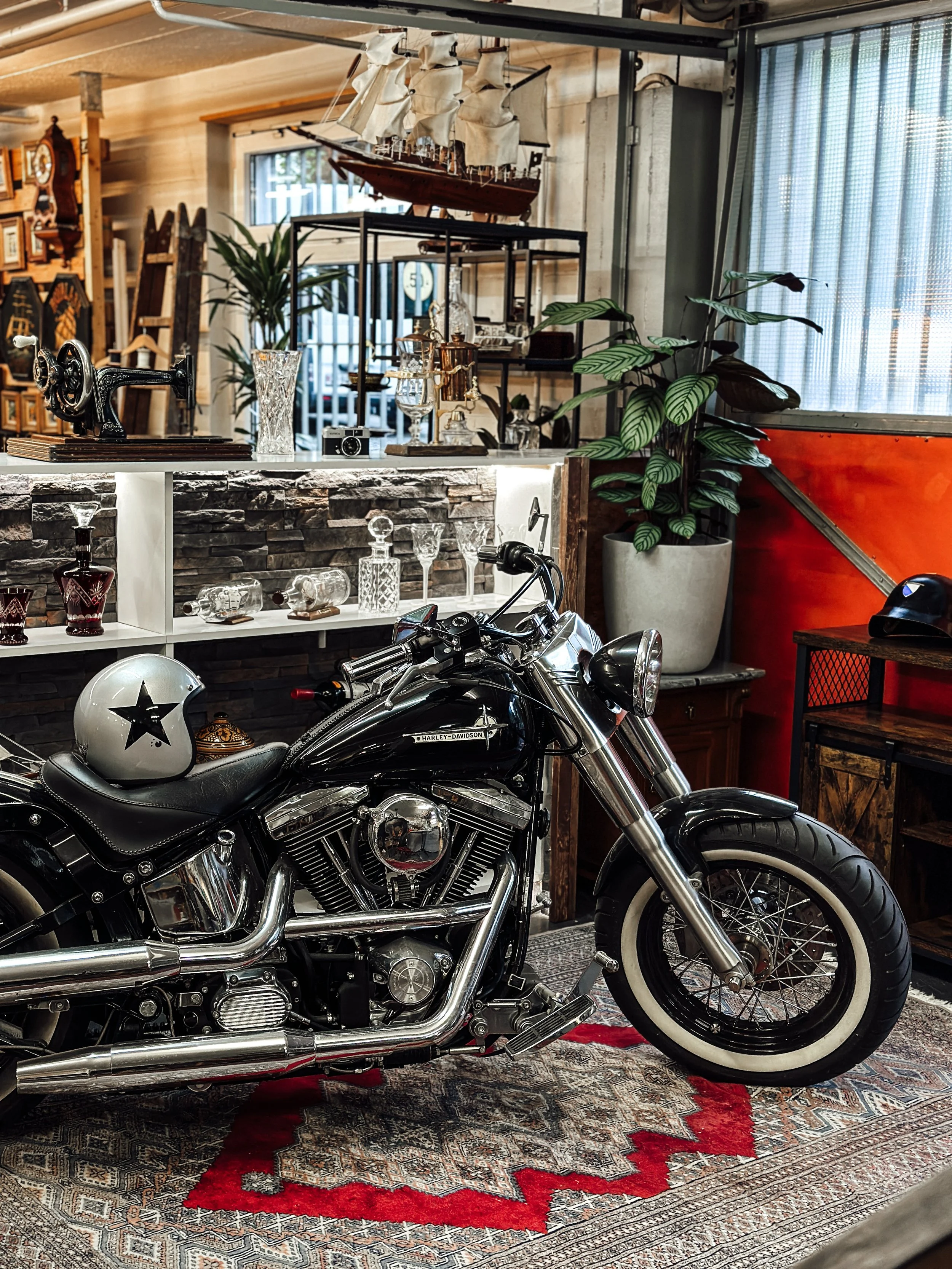 Motorrad in einem Raum mit antiken Gegenständen, darunter eine Nähmaschine, ein Modellschiff und diverse Gläser.