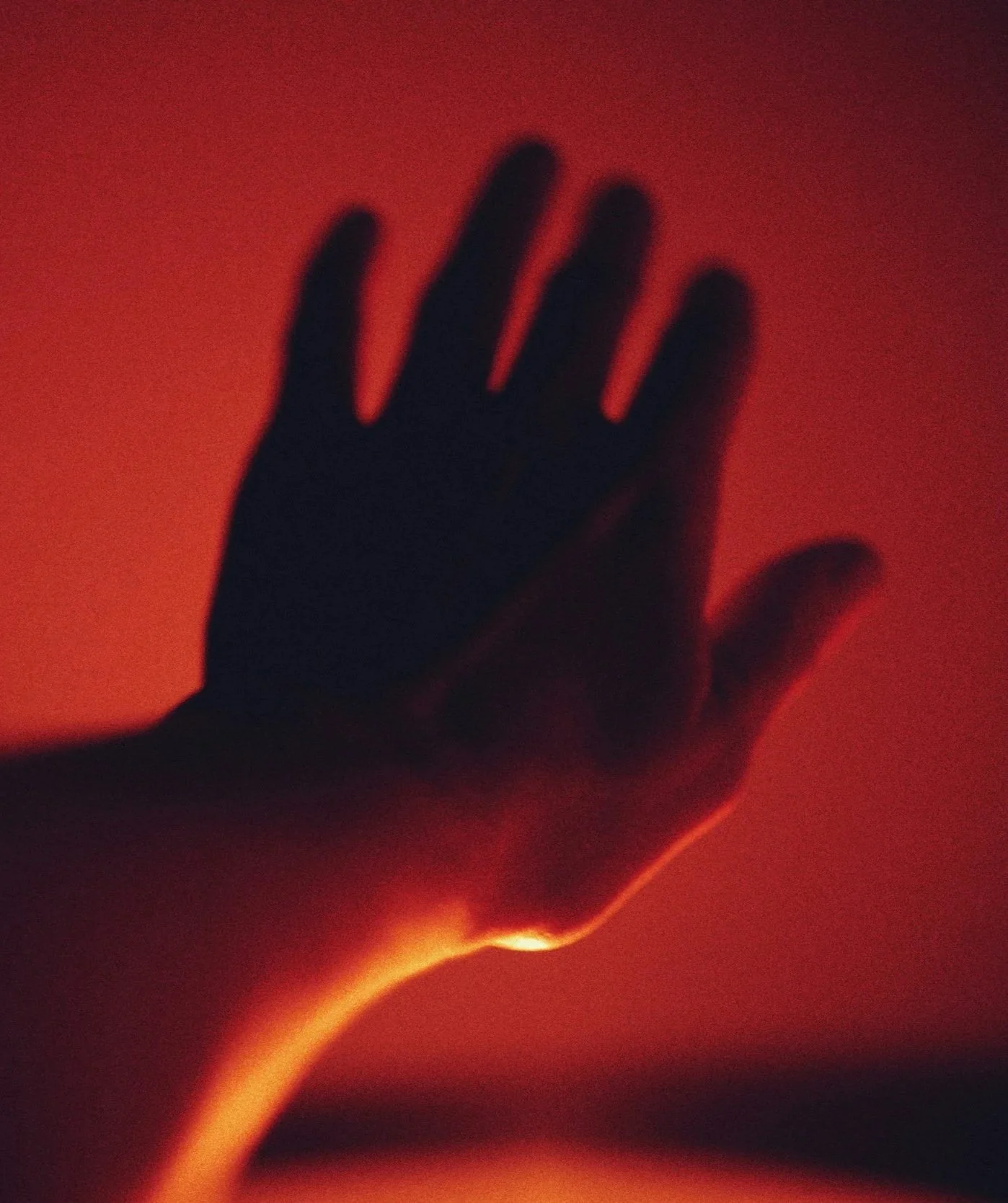 A hand reaching out against a glowing orange and red background, with the silhouette of the hand in shadow.