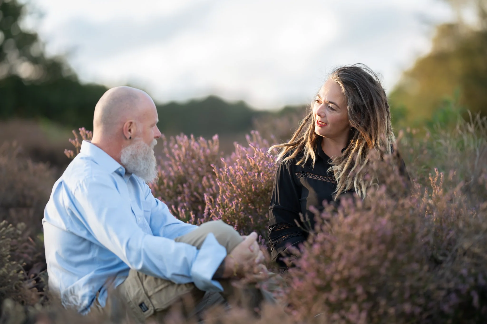 Twee mensen zitten in een veld met bloemen, ze kijken elkaar vriendelijk aan. Barbara Torres
