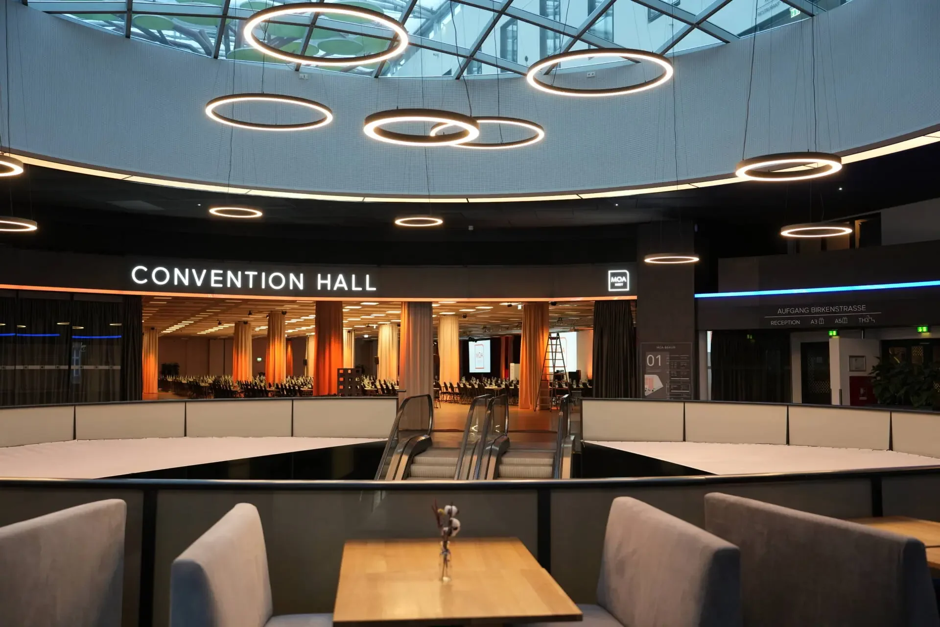 Interior view of a convention hall with warm lighting, seating arrangements, and a sign that reads 'CONVENTION HALL' at the entrance.