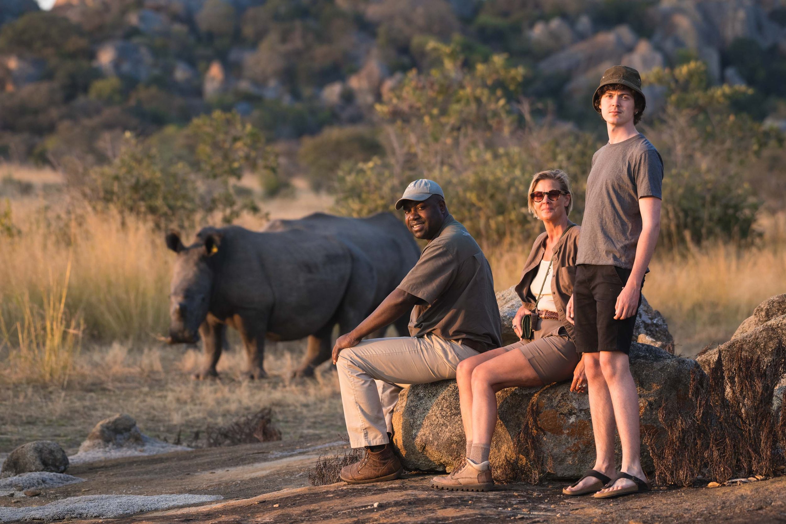 Three persons sitting near a rhino in Safari.
