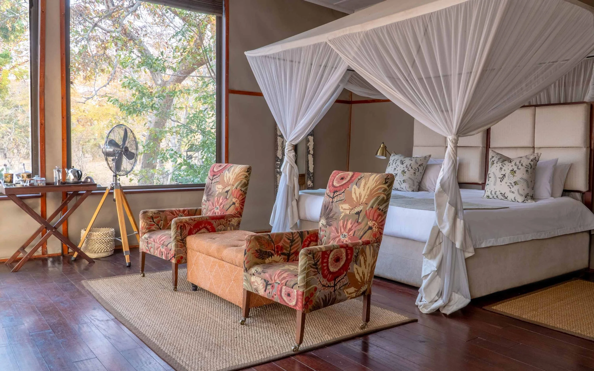 Bedroom with floral armchairs, a mosquito-net canopy and a large window at Khulu’s Retreat