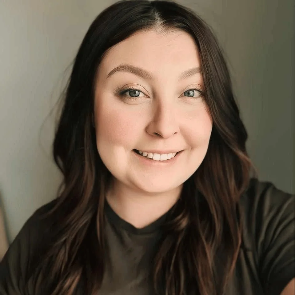 Smiling woman with long brown hair and a black shirt against a neutral background.