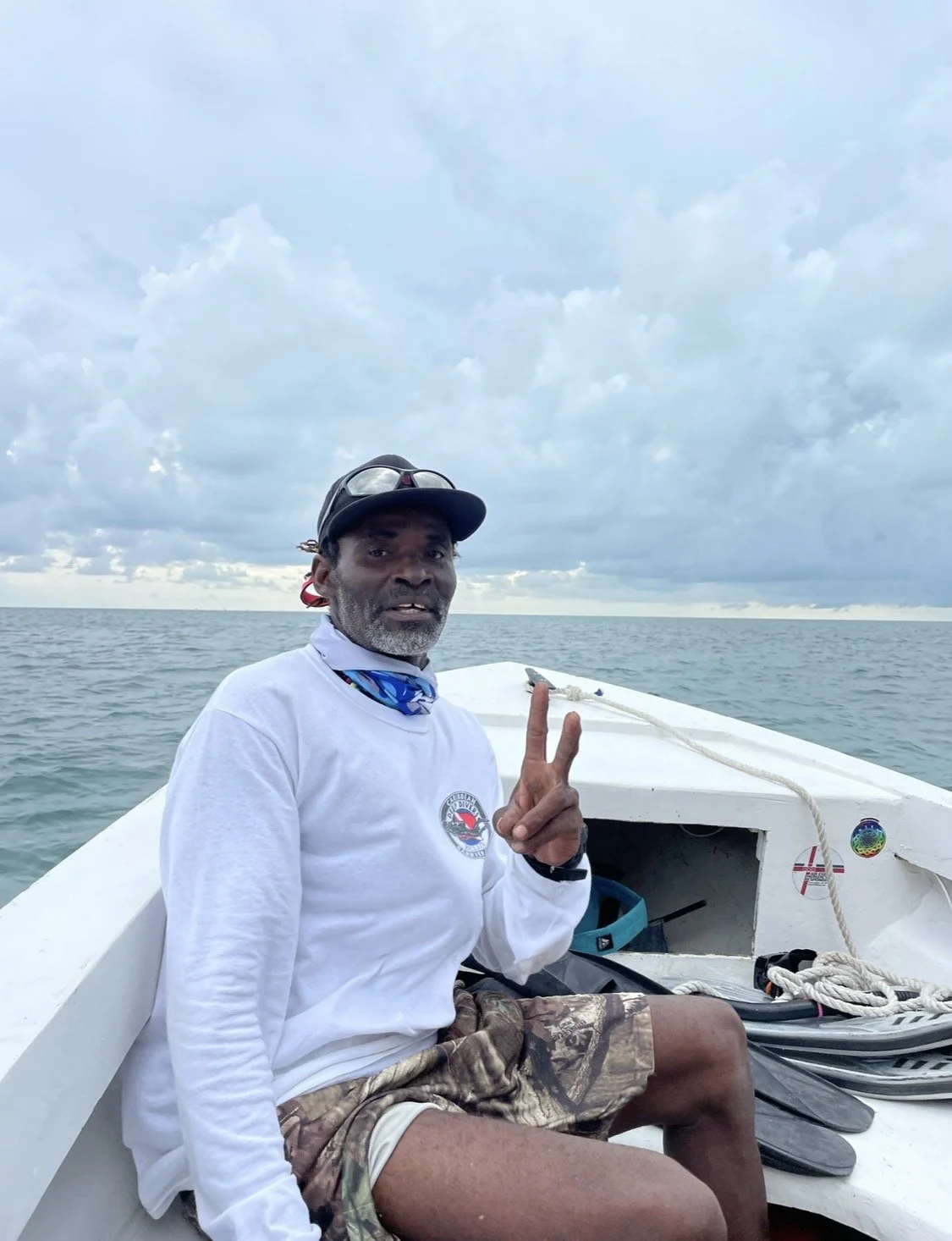 image of man on boat with baseball hat and white shirt on holding peace sign
