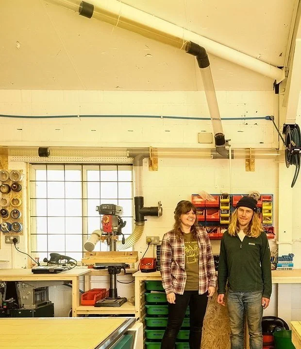 Two people standing in a workshop with various tools and equipment.