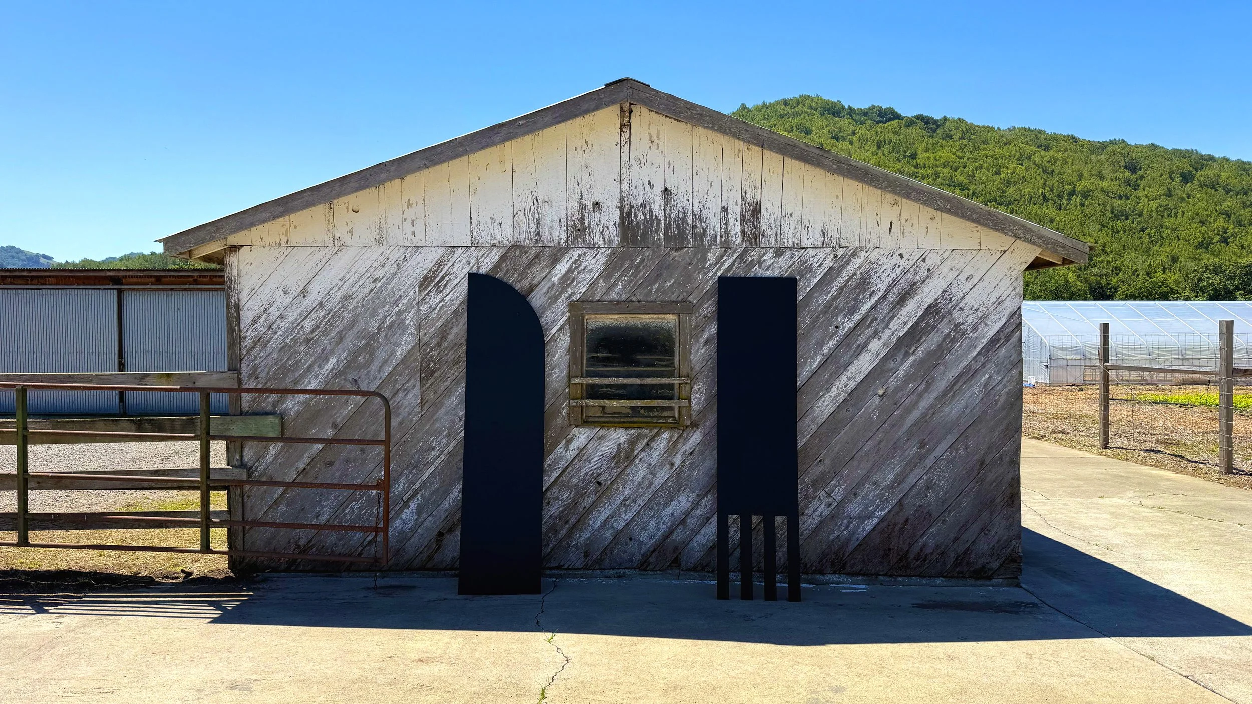 Large black fork and knife symbol signs from the Gastrodiplomacy logo standing against a worn wood walled barn on the Eames Ranch