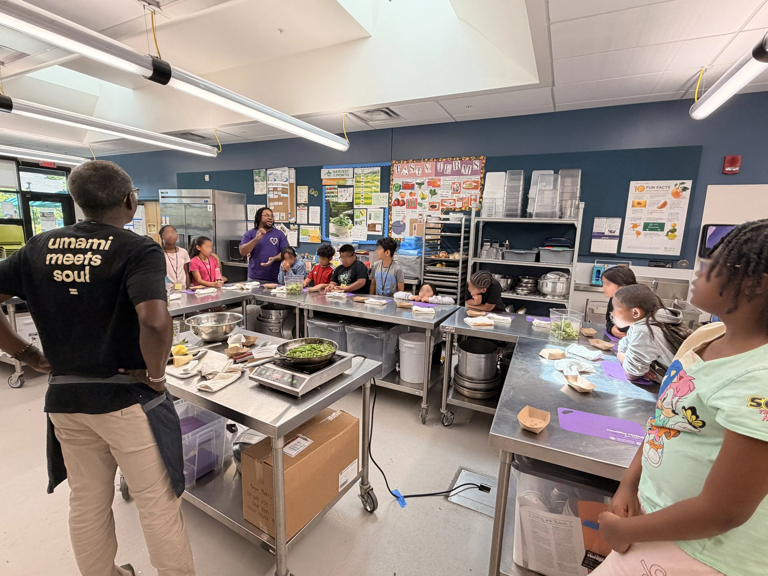 Chef Pierre teaches an Oakland school class a cooking demo in a commercial looking kitchen space