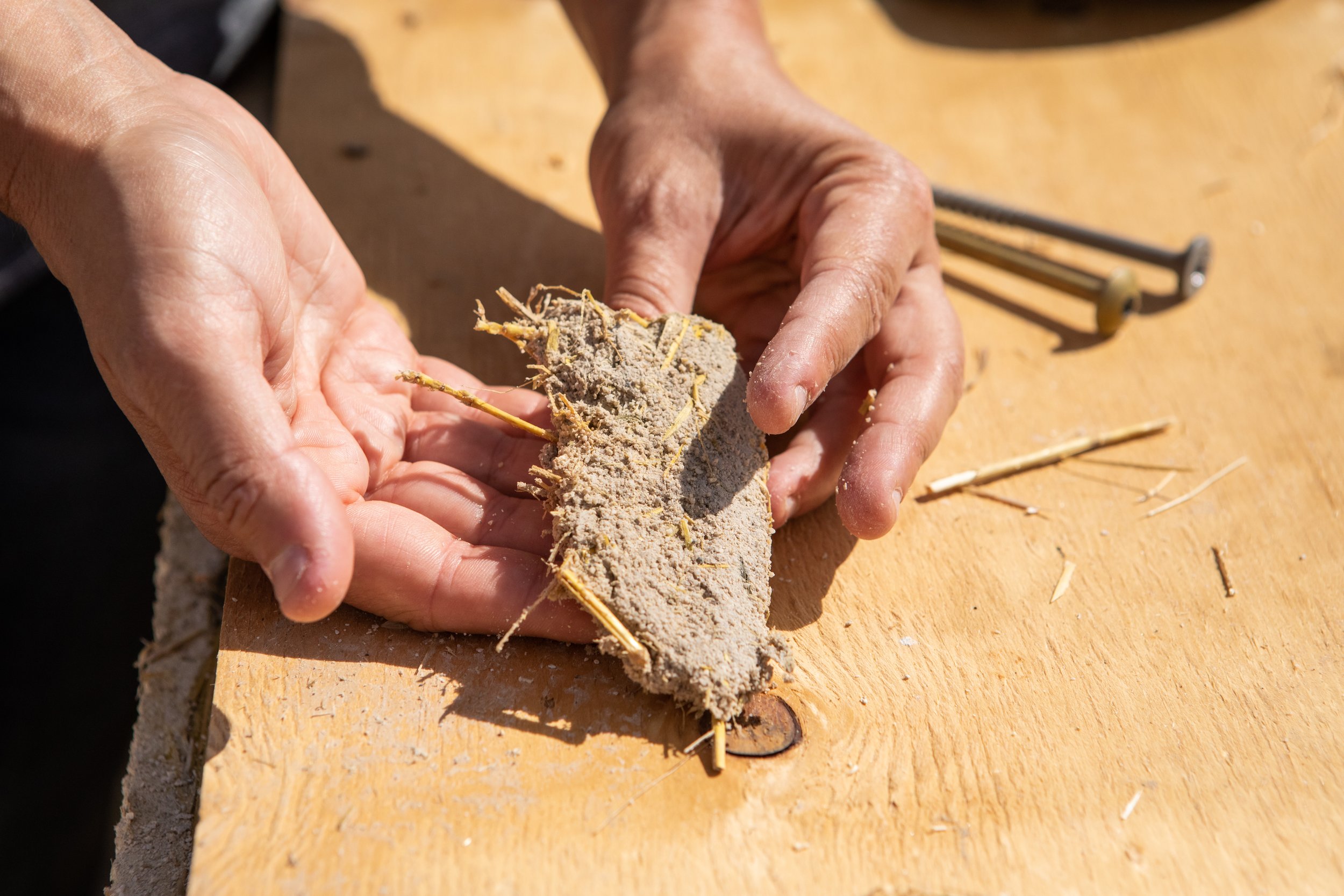 hands holding straw and plaster straw bale construction