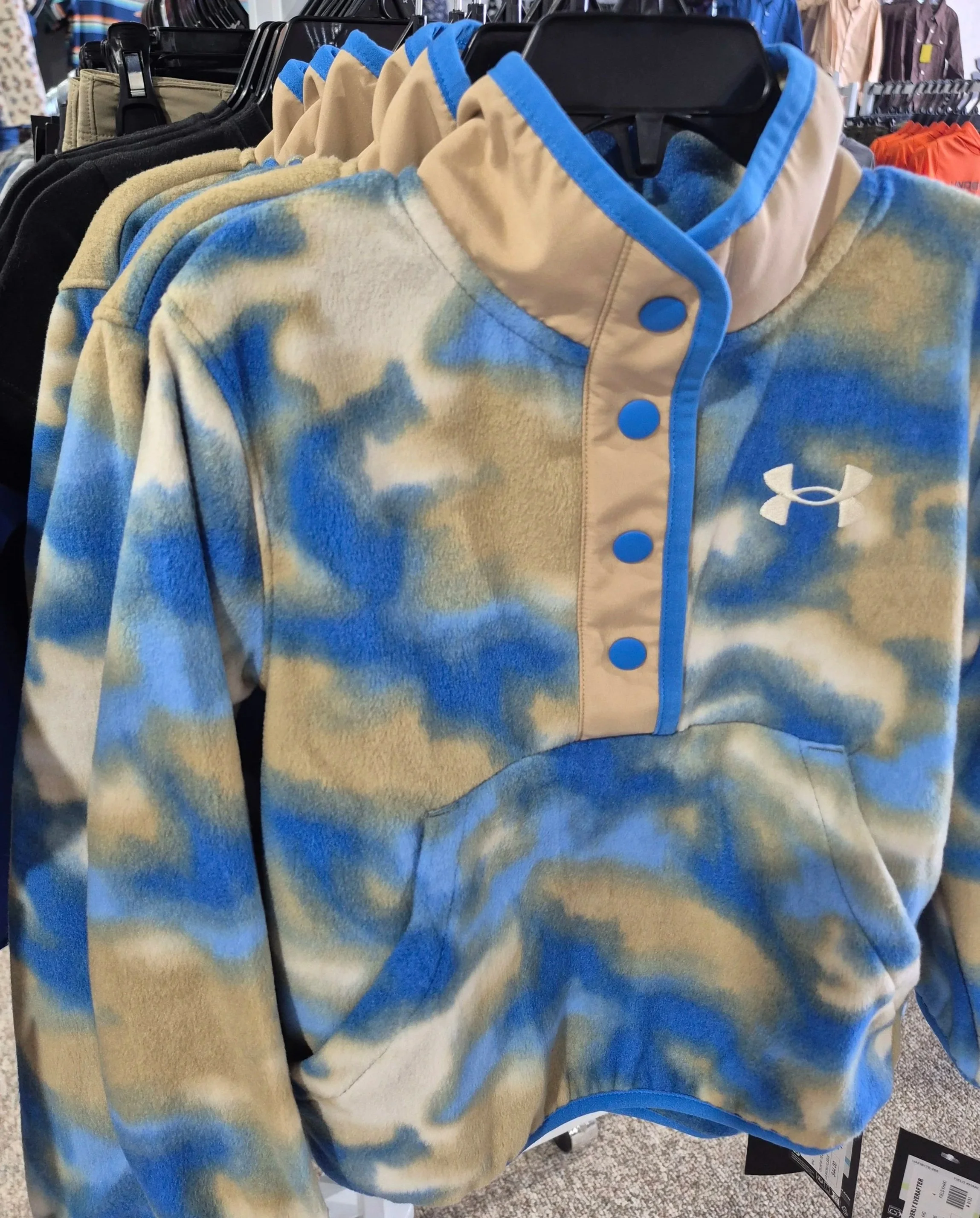 Blue and beige camouflage-patterned Under Armour fleece hoodie with a half-zip front, blue snap buttons, and a white Under Armour logo.