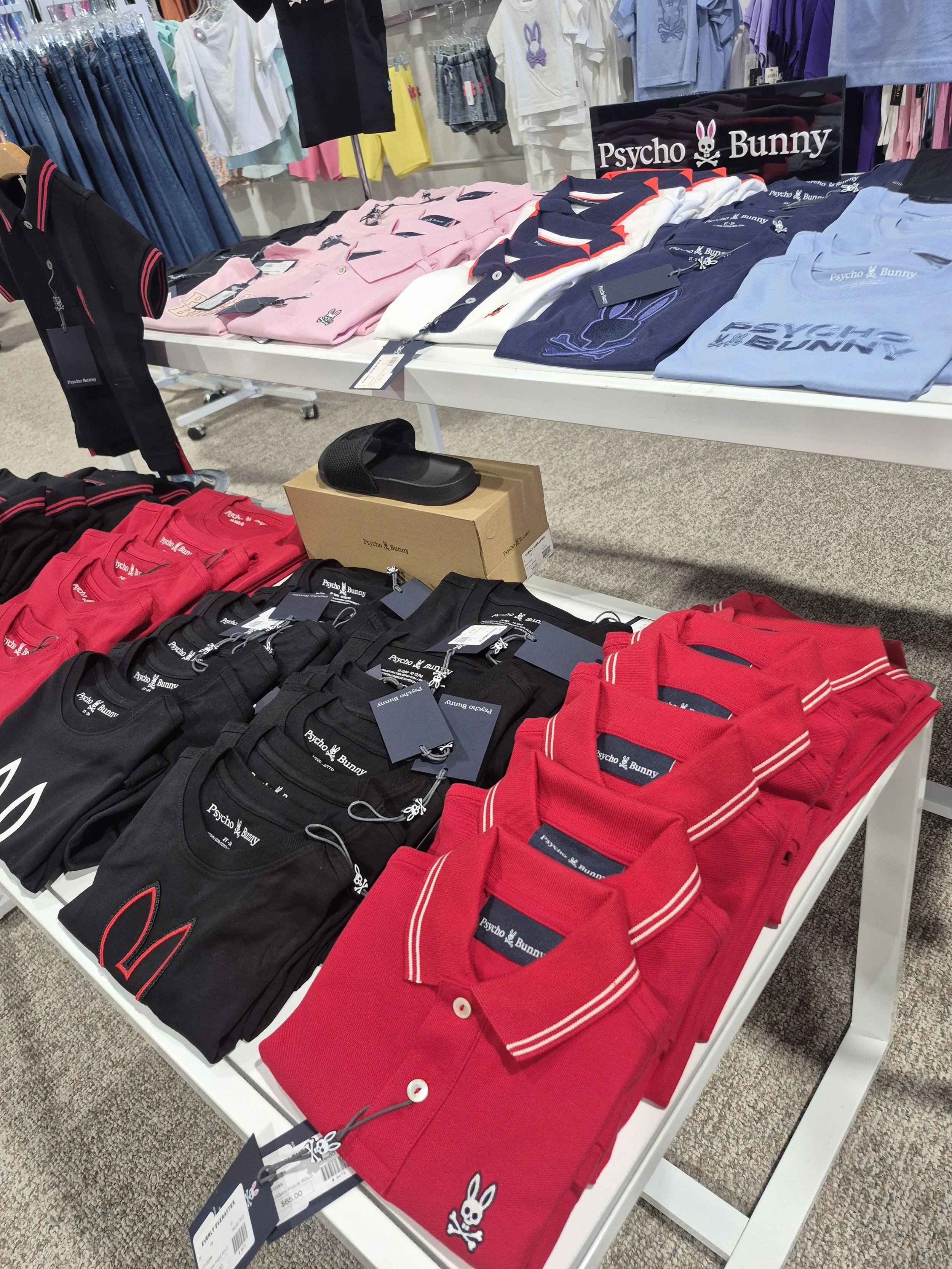 Display of Psycho Bunny branded polo shirts and T-shirts in various colors on store tables.