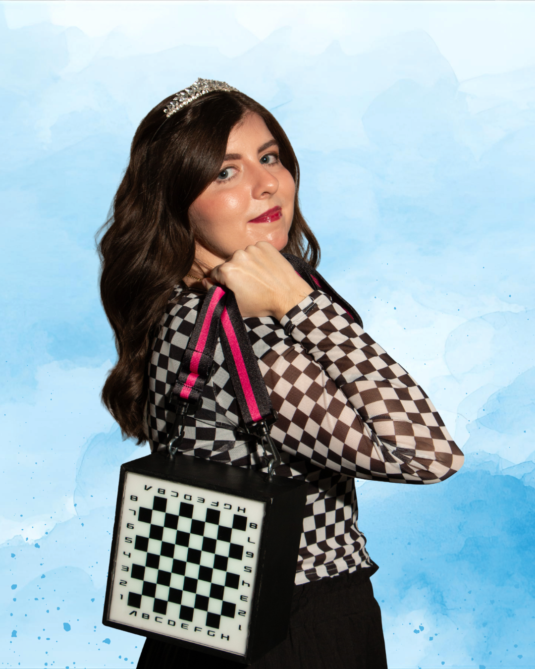 Woman with a checkered long sleeve shirt, dark wavy hair, wearing a tiara, holding a chessboard-shaped bag with pink straps, standing against a light blue watercolor background.