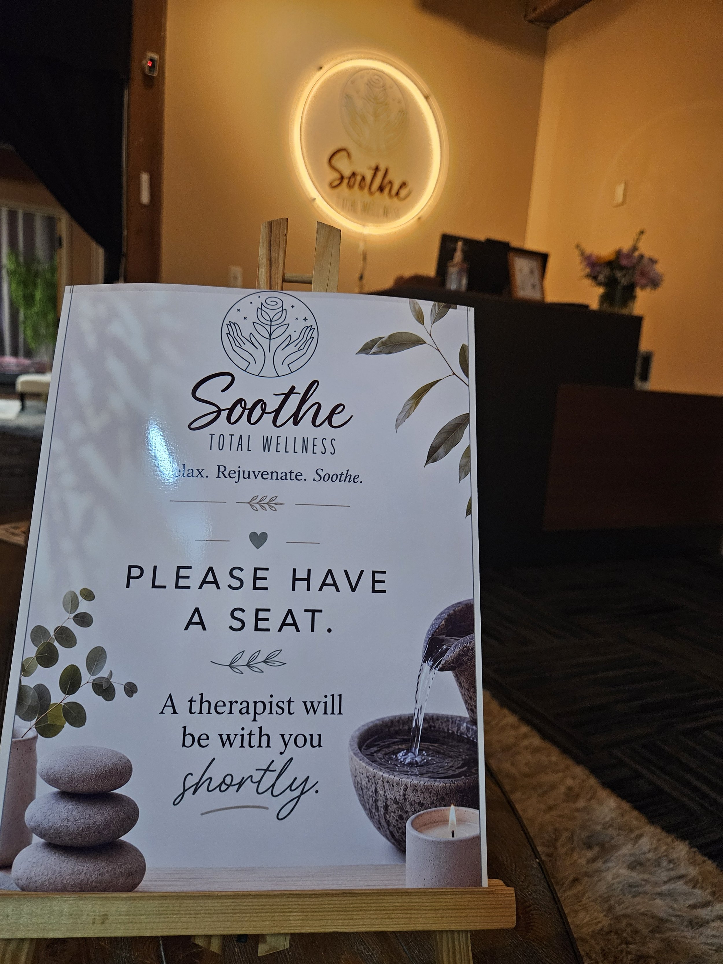 Sign at Soothe Total Wellness informing clietns to have a seat and a therapist will be with them shortly.