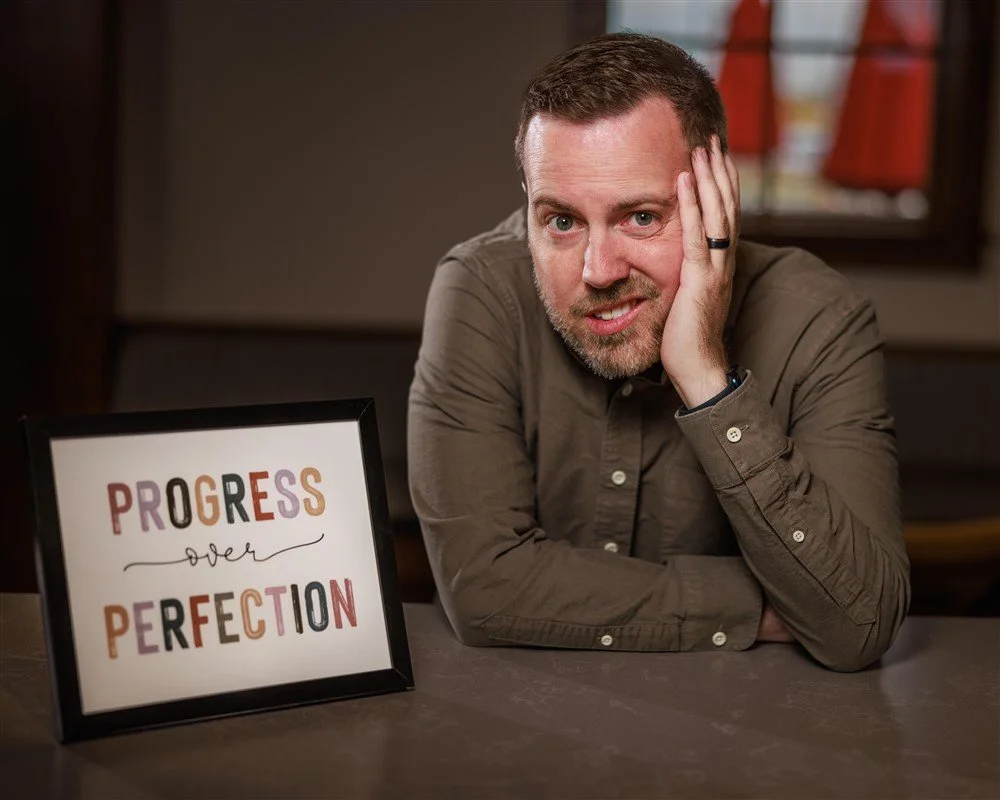 Shaun Boyle, Founder of TaberNext, making an anxious face next to a sign reading, "Progress over Perfection."