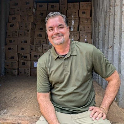 Smiling man with graying hair mustache and beard wearing khaki colored shirt and tan pants