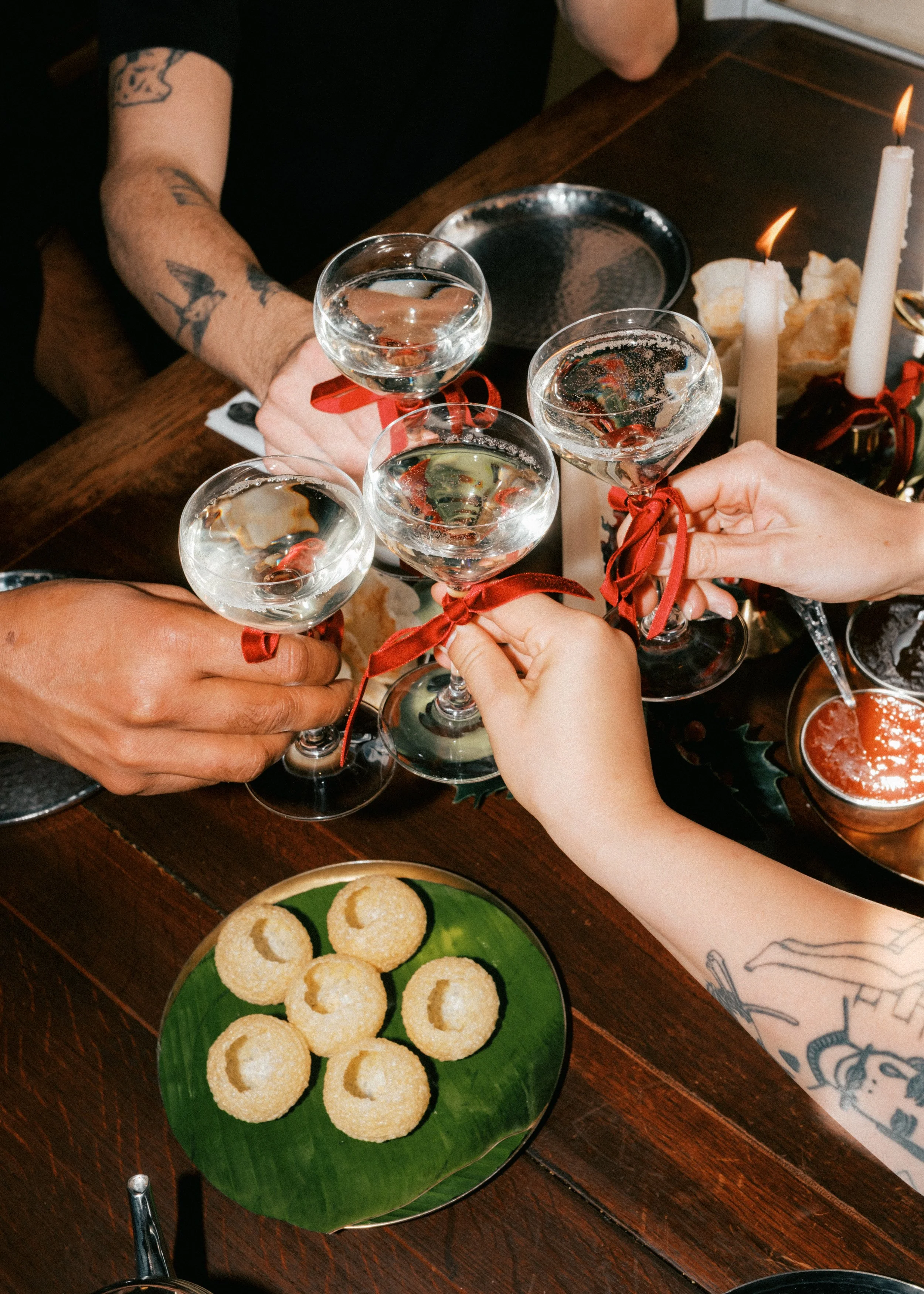 People raising glasses of champagne in a toast, with a plate of cookies and candles on a table.