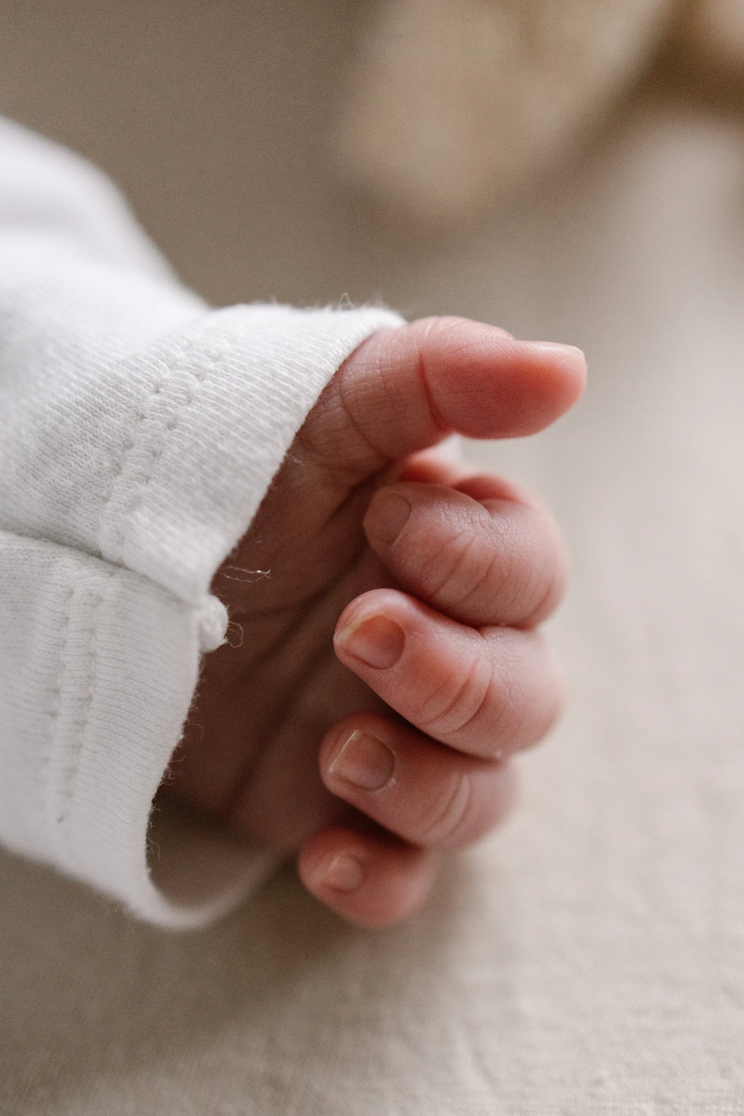A close-up of a newborn hand holding another person's finger, with the sleeve of a white shirt visible. newbornshoot, newbornfotograaf haarlem, newborn shoot thuis. 