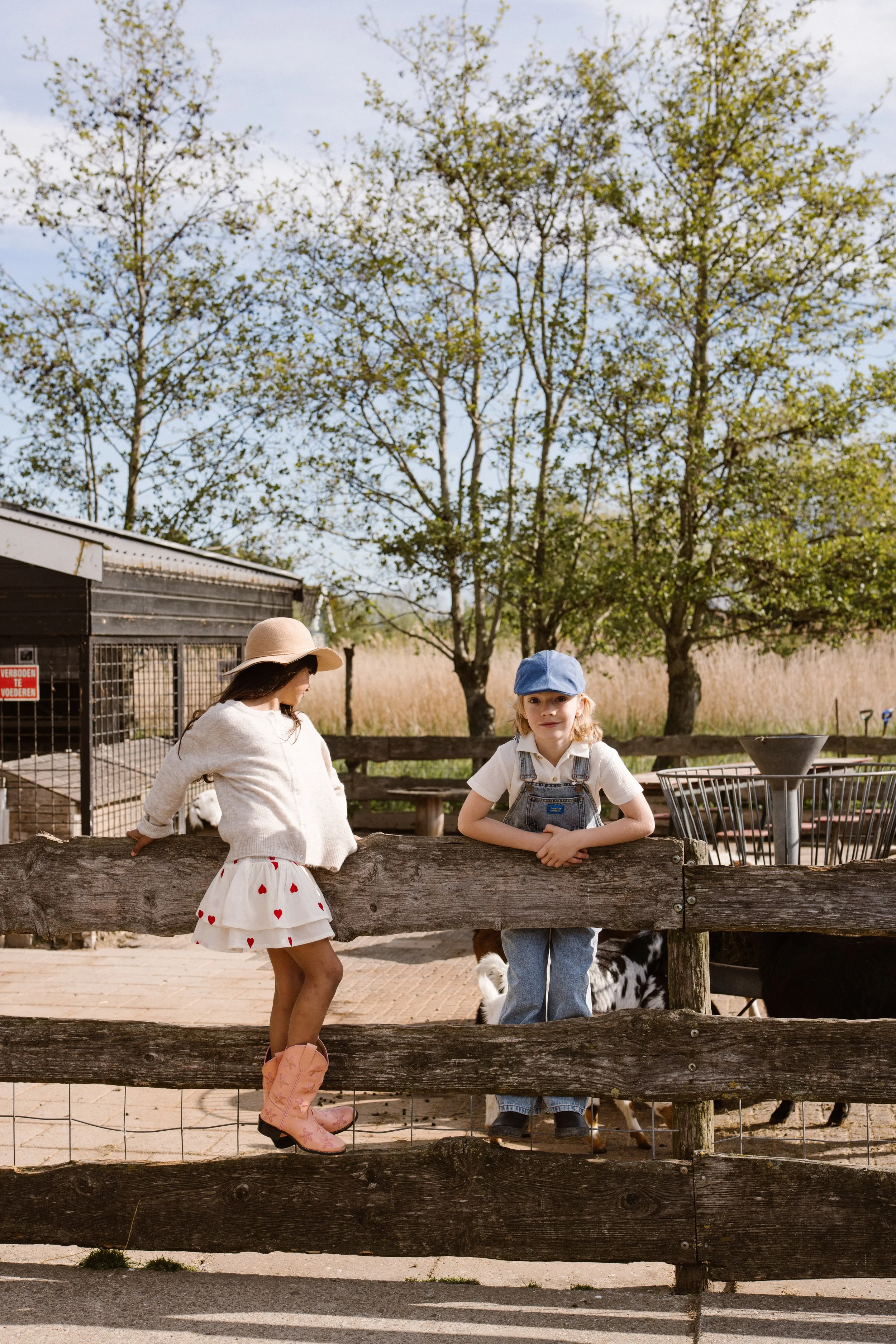 a young girl and boy in a petting zoo, standing behind a wooden fence. fashion shoot, lifestyle shoot, brandshoot, lieneloe fashion haarlem