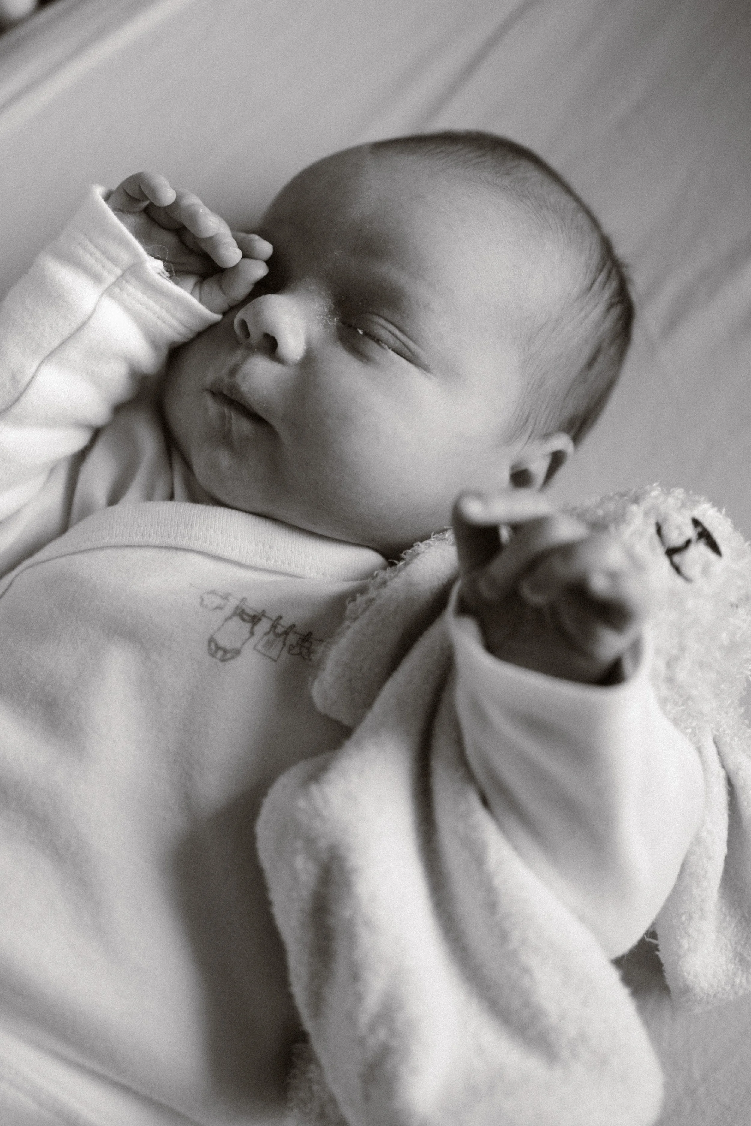 Black and white photo of a newborn baby. The baby is peacefully sleeping, with a small hand near the face and a slightly open mouth. newbornshoot, newbornfotograaf haarlem, newborn shoot thuis. 