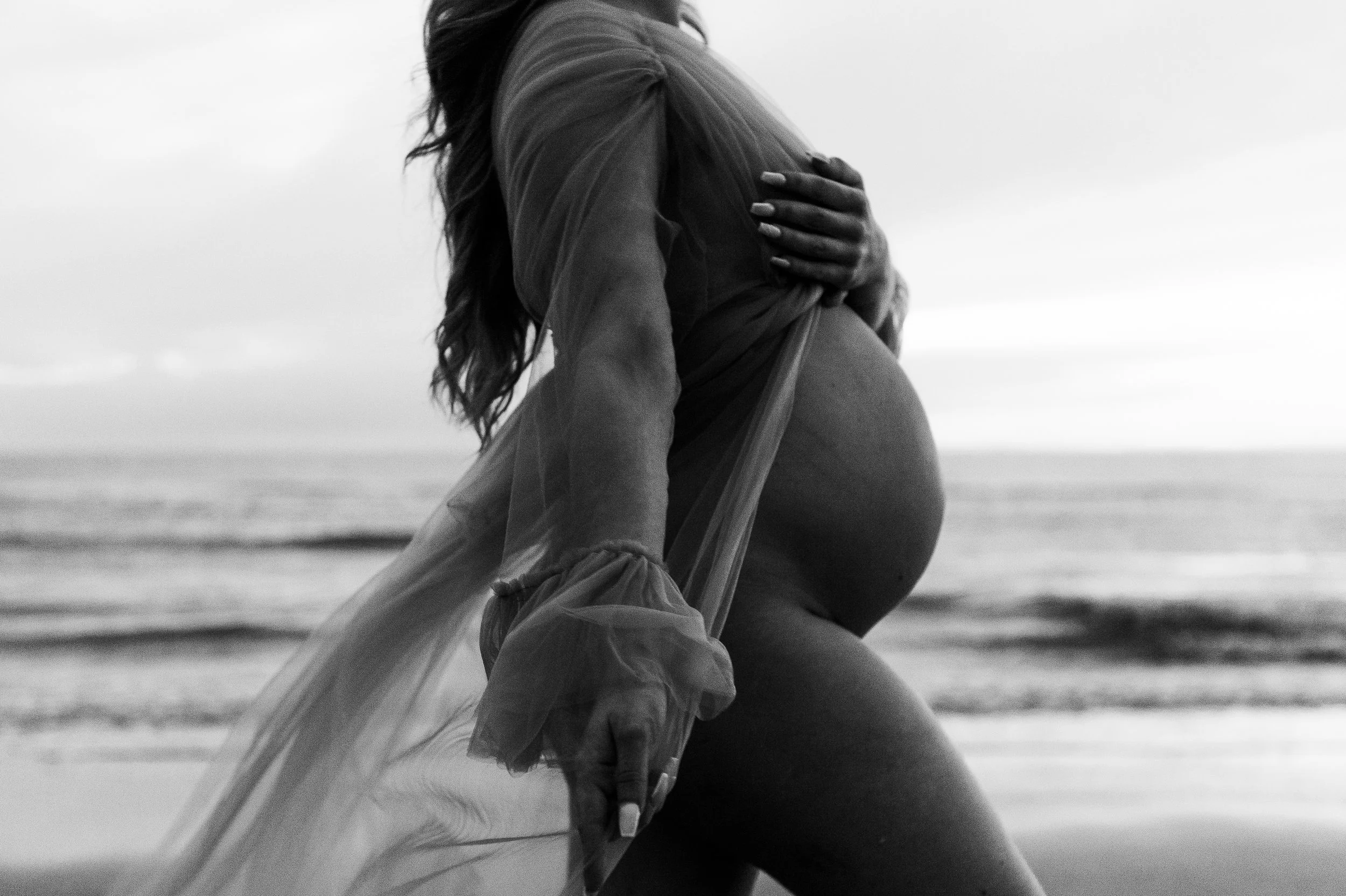 A pregnant woman wearing a white dress standing outdoors at sunset, bij ijmuiden aan zee, ijmuiderslag. lifestylefotografie, lifestyleshoot, zwangerschapsfotografie, zwangerschapsshoot, shoot duinen, fotograaf haarlem. 