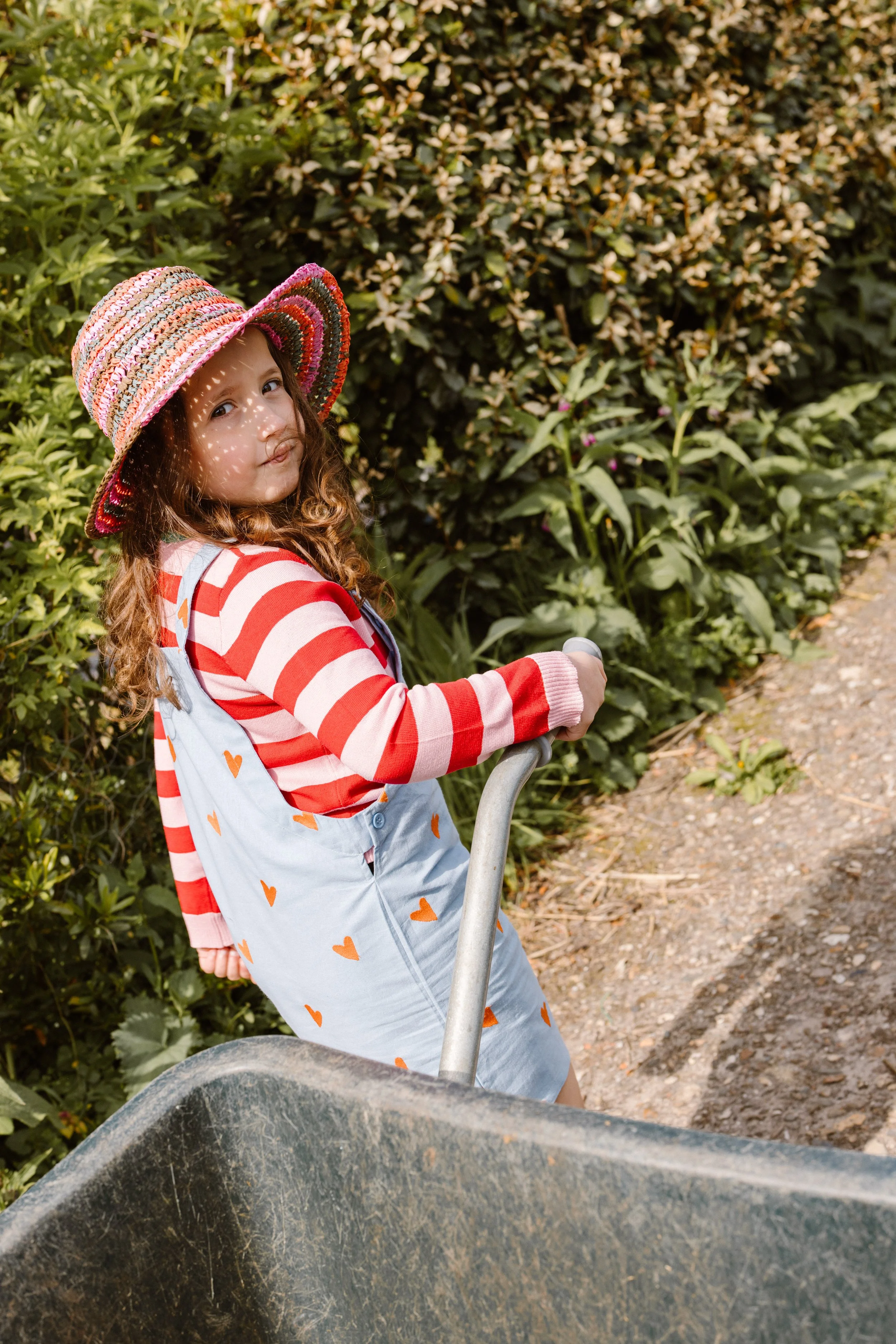 A young girl with curly brown hair wearing a colorful wide-brimmed hat and a red and white striped long sleeve shirt. fashion shoot, lifestyle shoot, brandshoot, lieneloe fashion haarlem