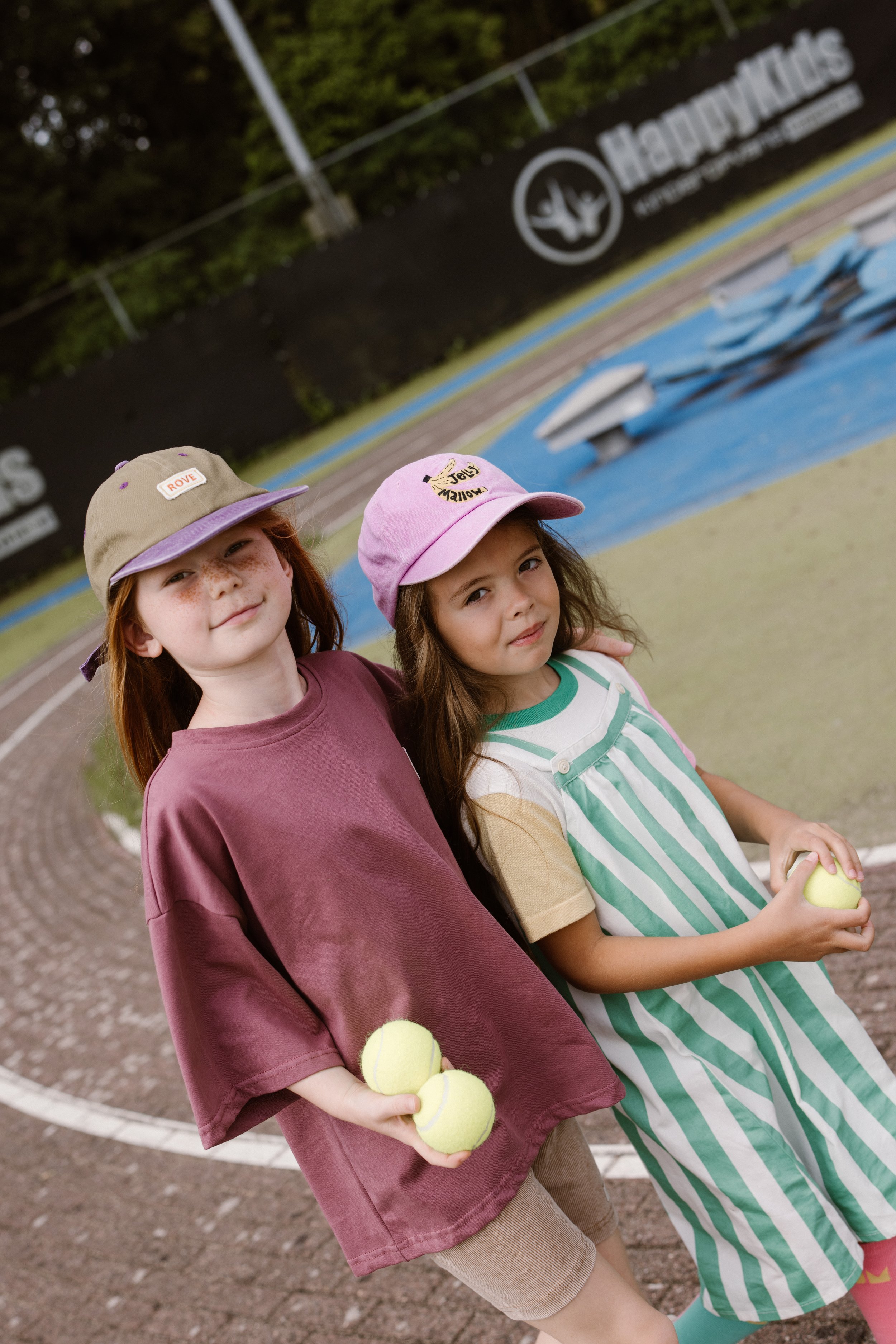 Two young girls standing close together near a tennis court, holding tennis balls. fashion shoot, lifestyle shoot, brandshoot, lieneloe fashion haarlem