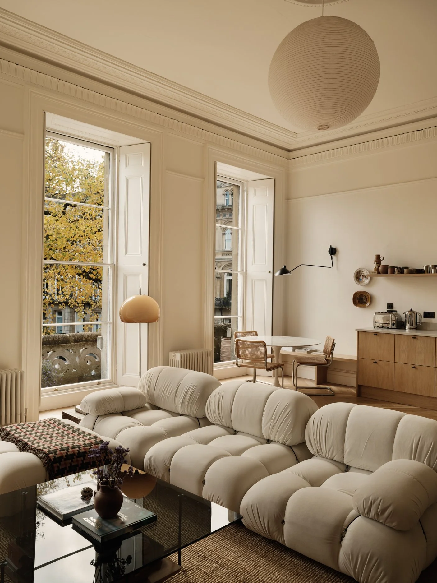 Living room with large windows, white sofa, coffee table, and dining area in the background.