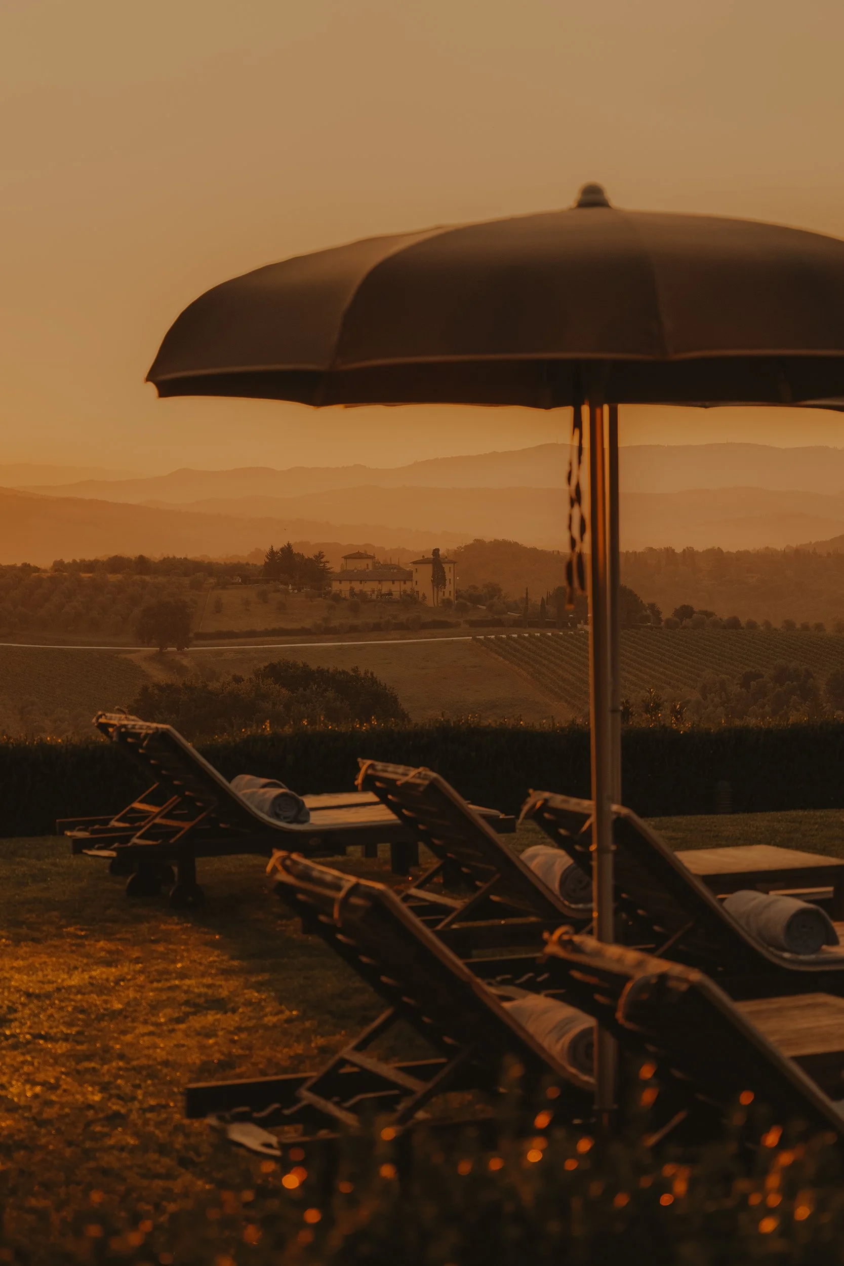 Sunset view of lounge chairs and umbrella overlooking rolling hills and vineyards.