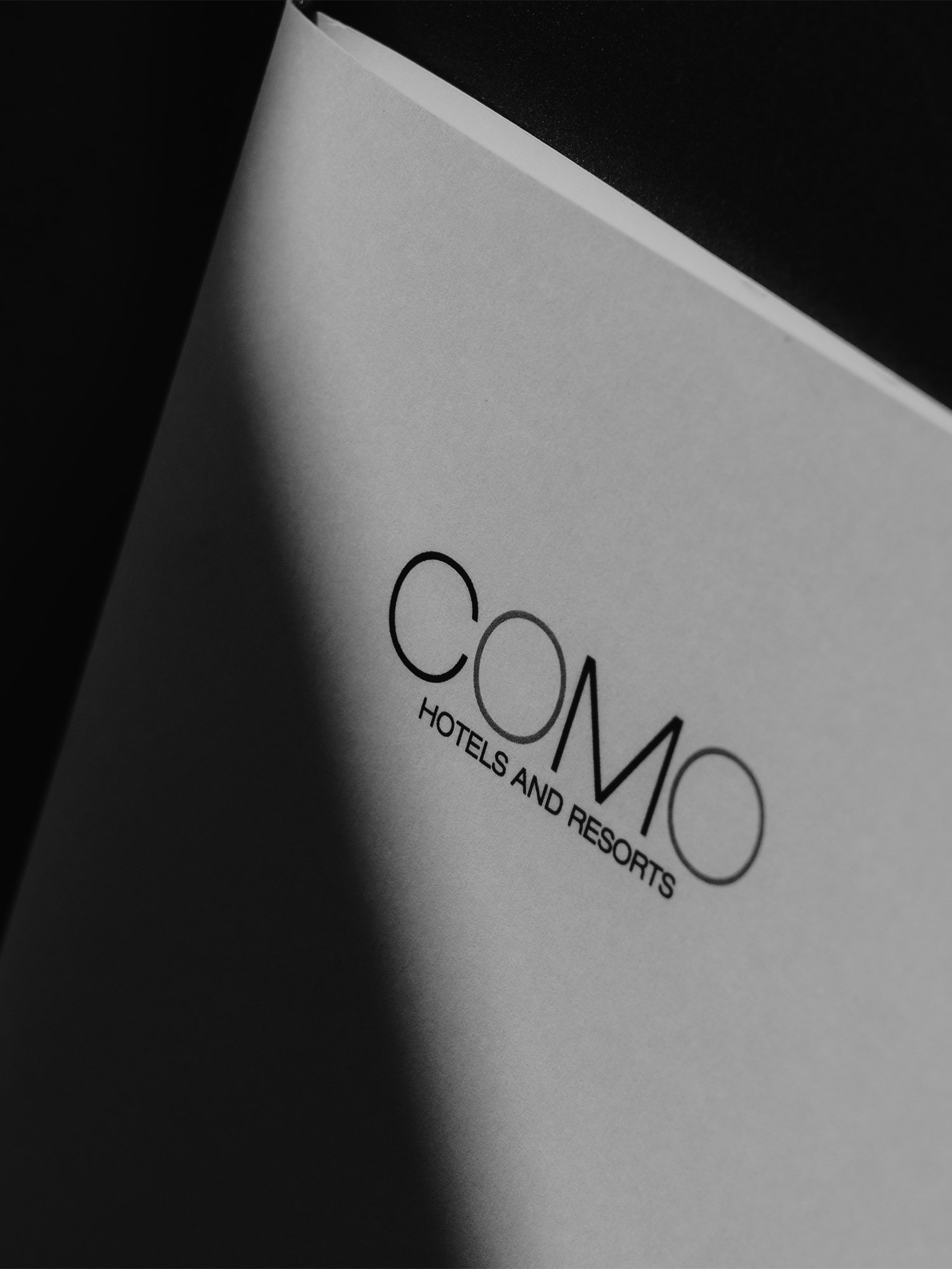 Close-up of a printed page with the logo of COMO Hotels and Resorts, with shadows created by lighting.