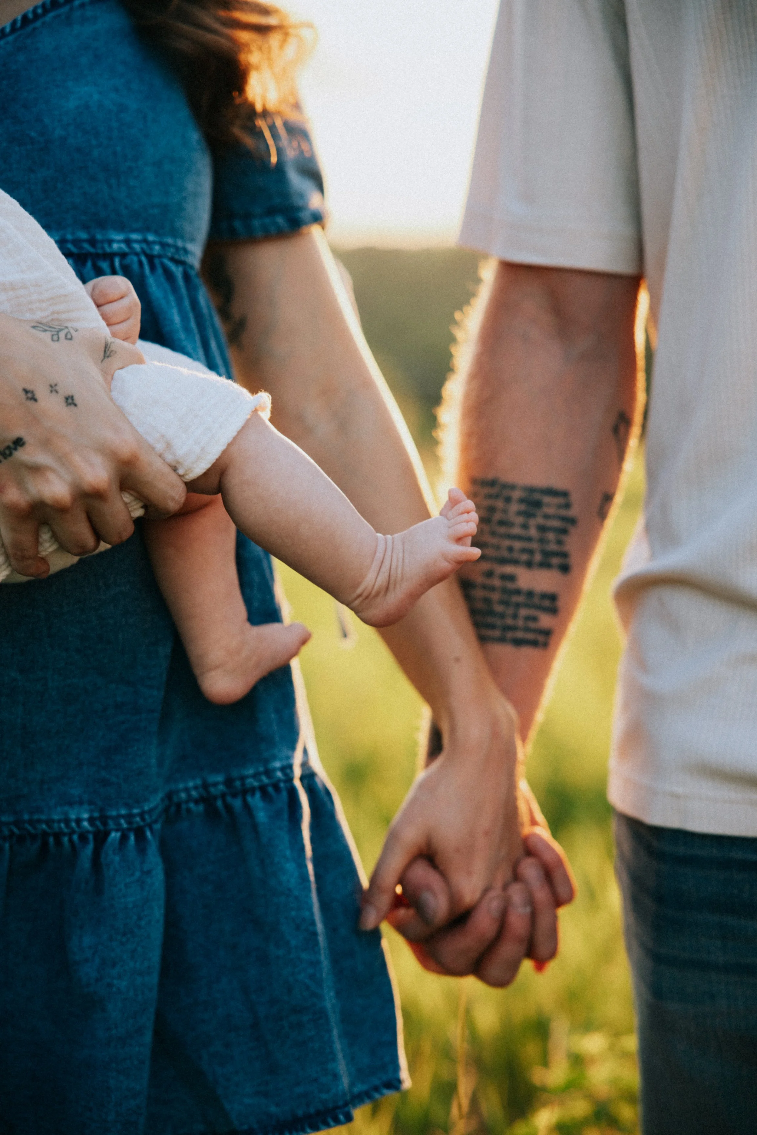 Close-up of a couple holding hands with a child between them outdoors, with warm sunlight.