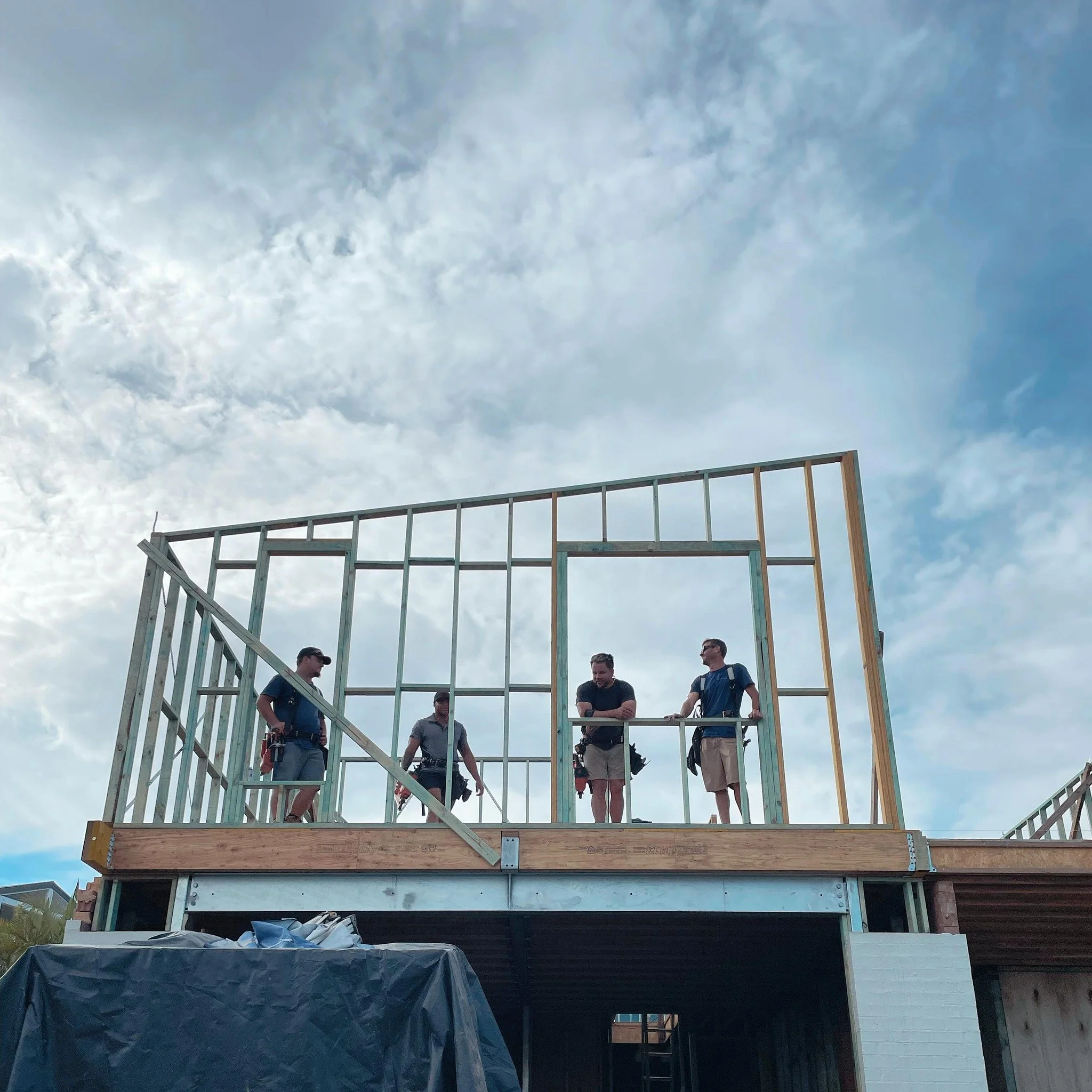 Home renovation where new meets old, showing construction workers on the second floor beside a newly framed wall and an open window.