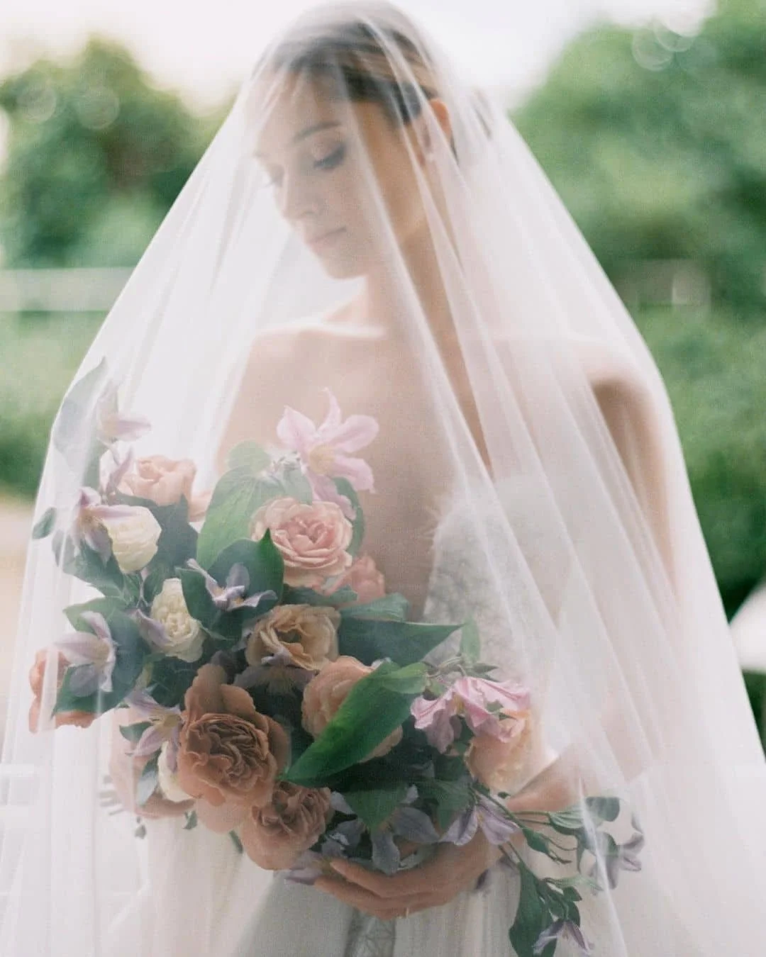 Bride in wedding dress holding a bouquet of flowers under a translucent veil.