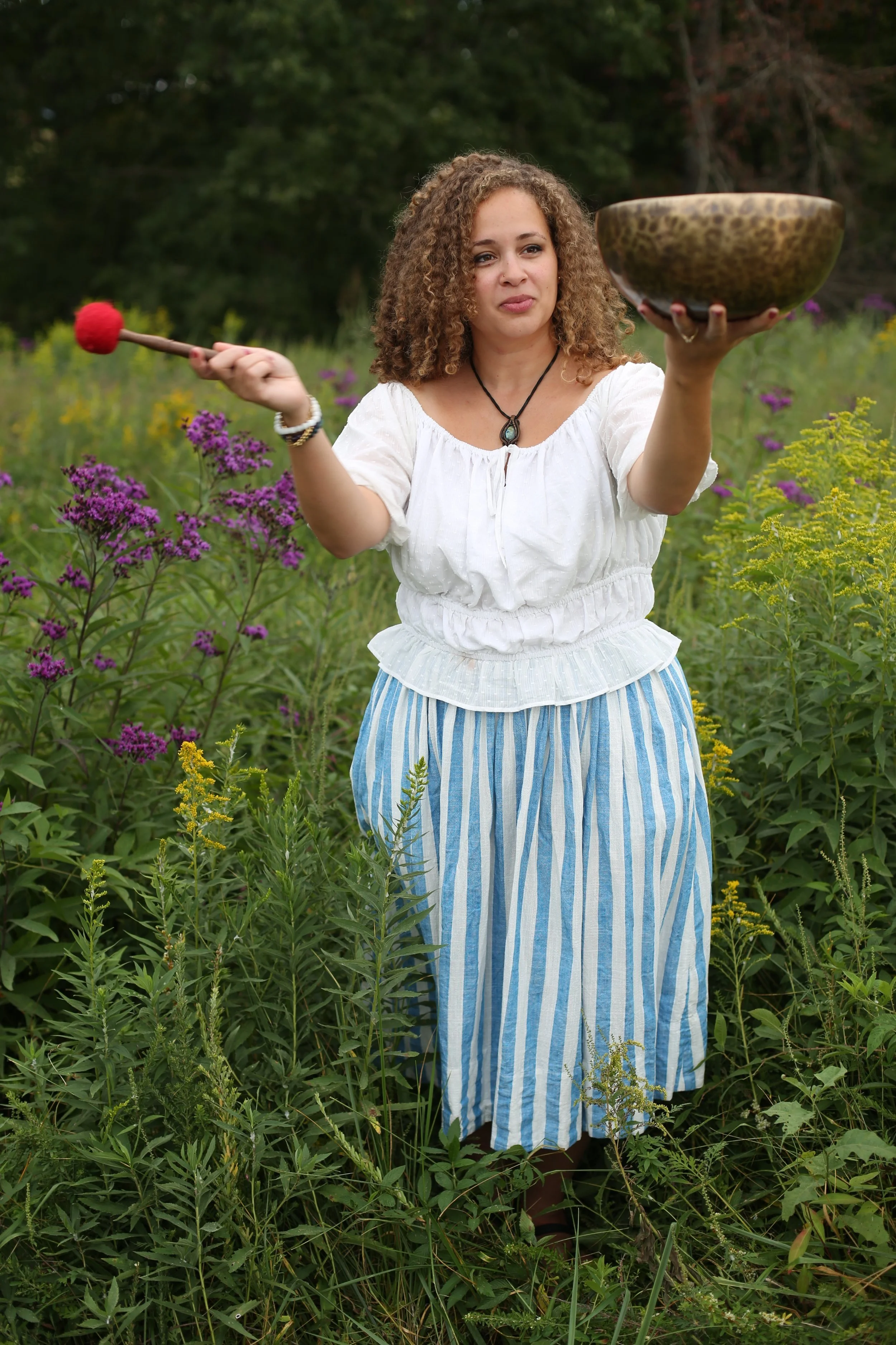 sound healing practitioner tapping tibetan singing bowl in field of flowers