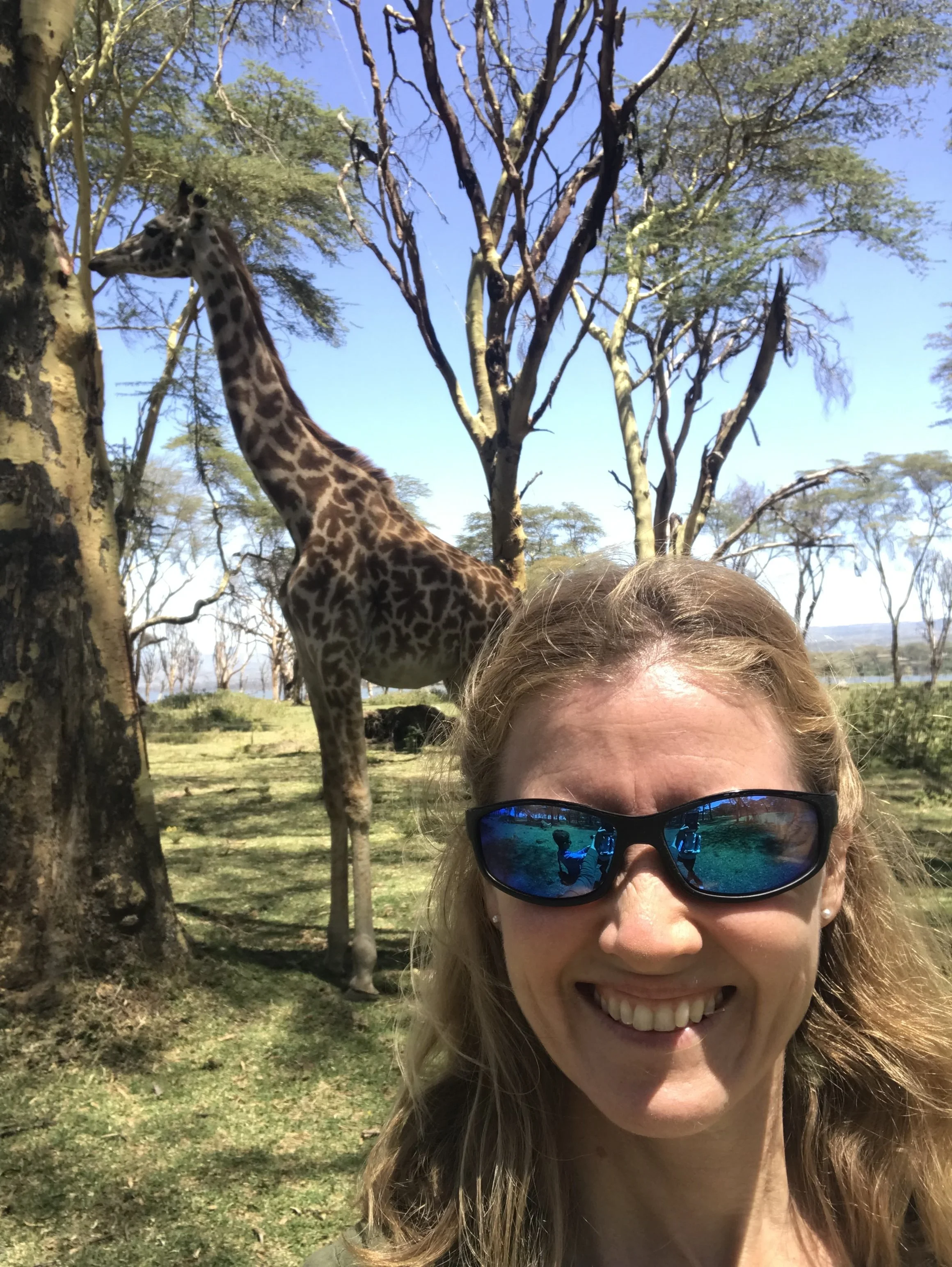 Woman in sunglasses poses in front of a giraffe.
