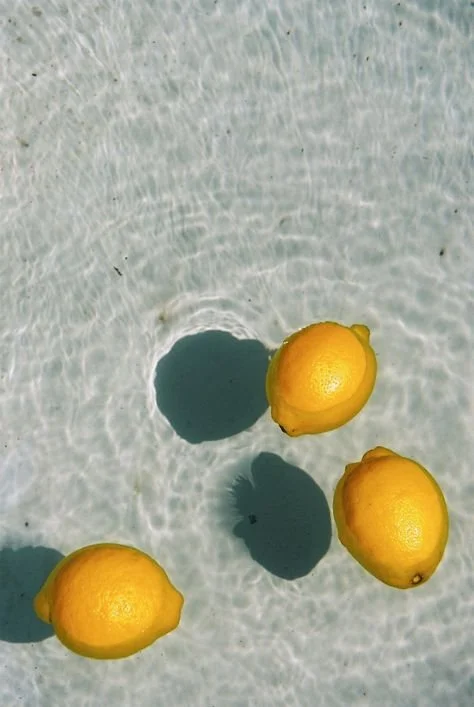 Four lemons floating in clear water, casting shadows.