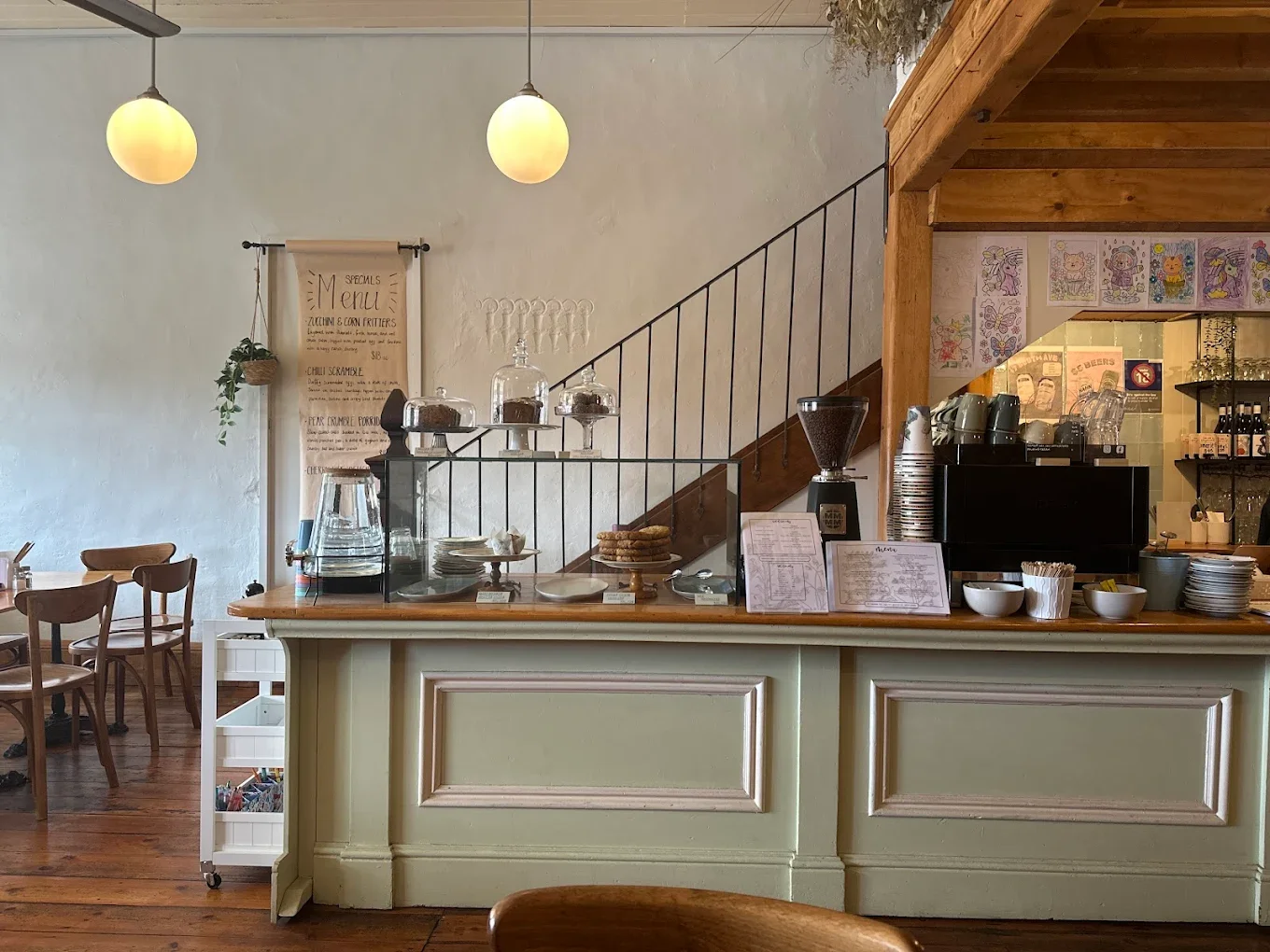 Interior of a cozy cafe with a counter displaying baked goods, cookware, and menus, featuring wooden accents and minimalistic decor.