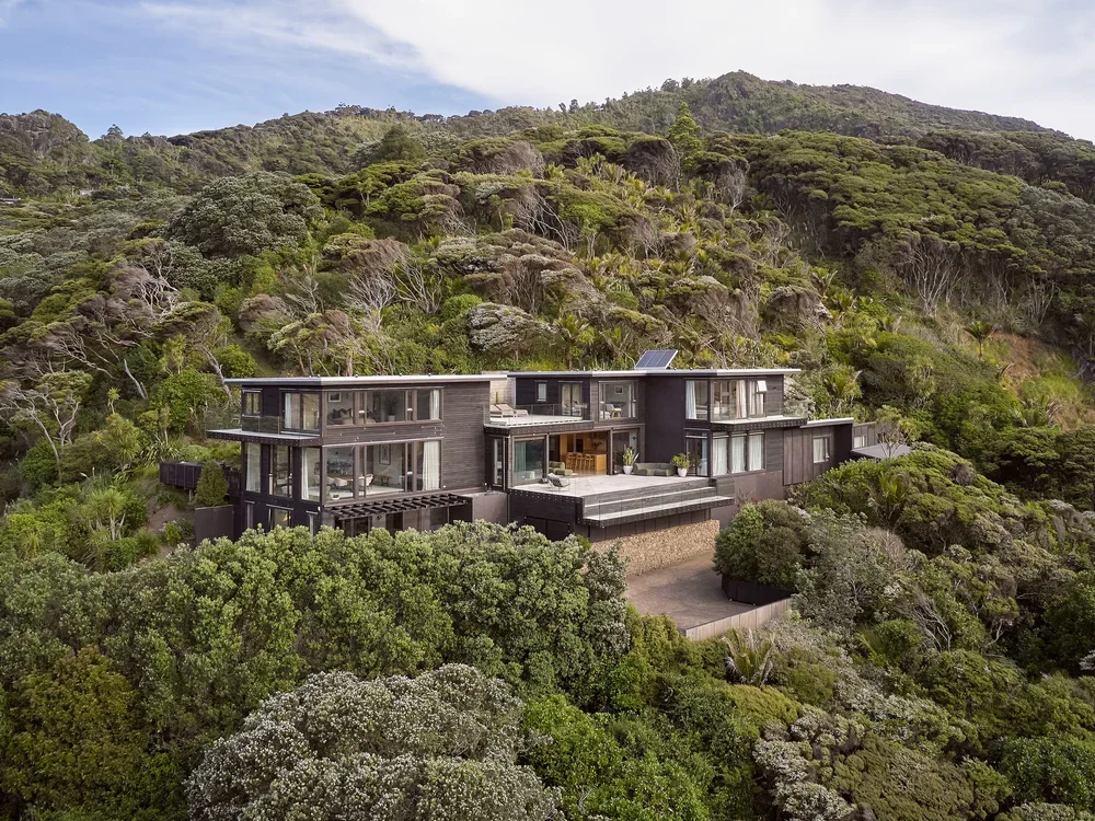 Modern house built on a hillside surrounded by dense green trees and shrubs.