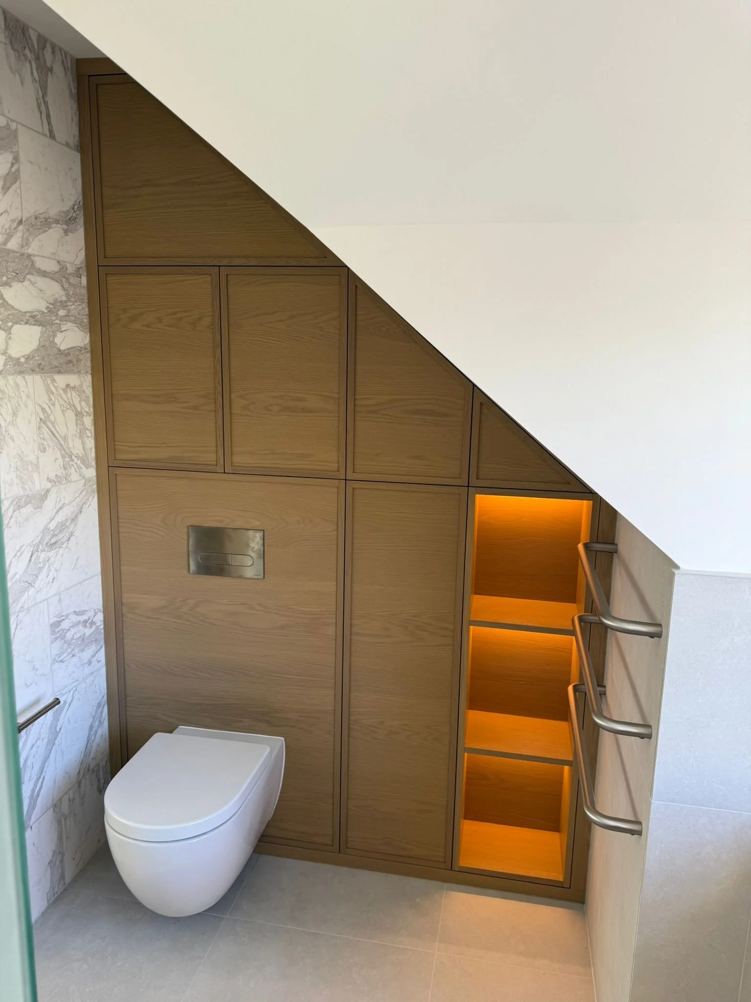 Modern bathroom with a wall-mounted toilet, wooden storage cabinets with illuminated shelves, and stone wall accents.