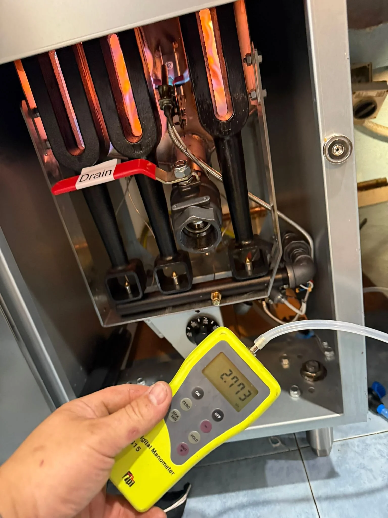 Close-up of a refrigeration or cooling system with black evaporator coils, a red drain valve, and a digital manometer reading 270.3.